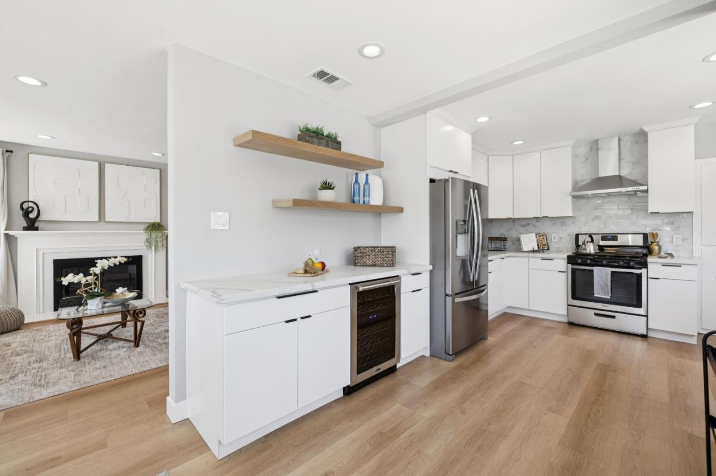 Bright white kitchen with stainless steel appliances, a large peninsula, and an adjoining living area with fireplace.
