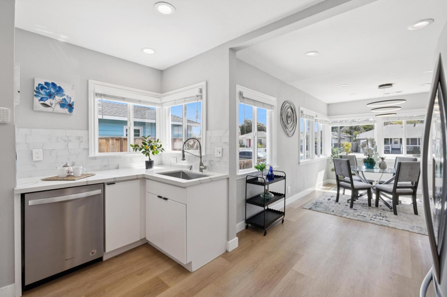 Bright white kitchen with corner windows opening to a glass-table dining area.