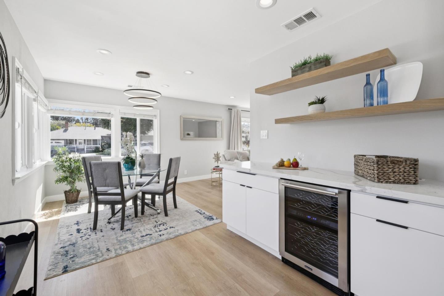 Kitchen and dining area with a built-in wine refrigerator and glass table beside large windows.