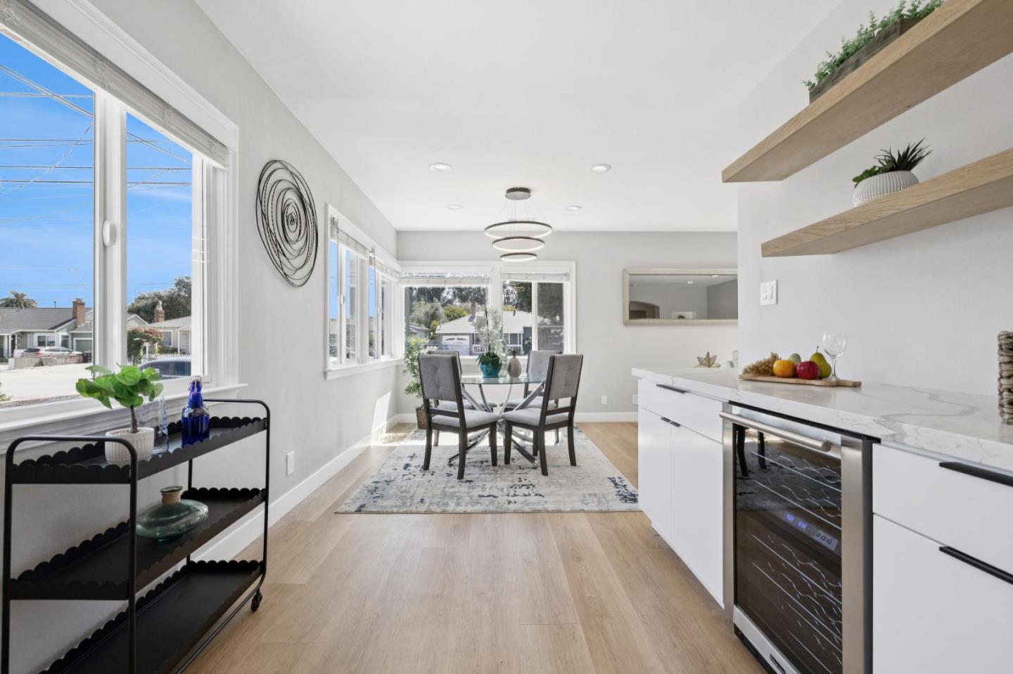 Kitchen and dining area with a marble-look island, floating shelves, and a glass table by large windows.