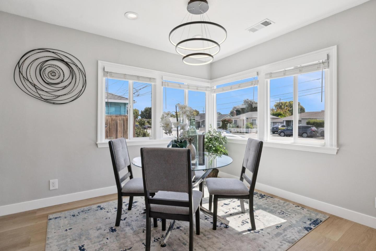 Dining room with a round glass table, upholstered chairs, and large corner windows.