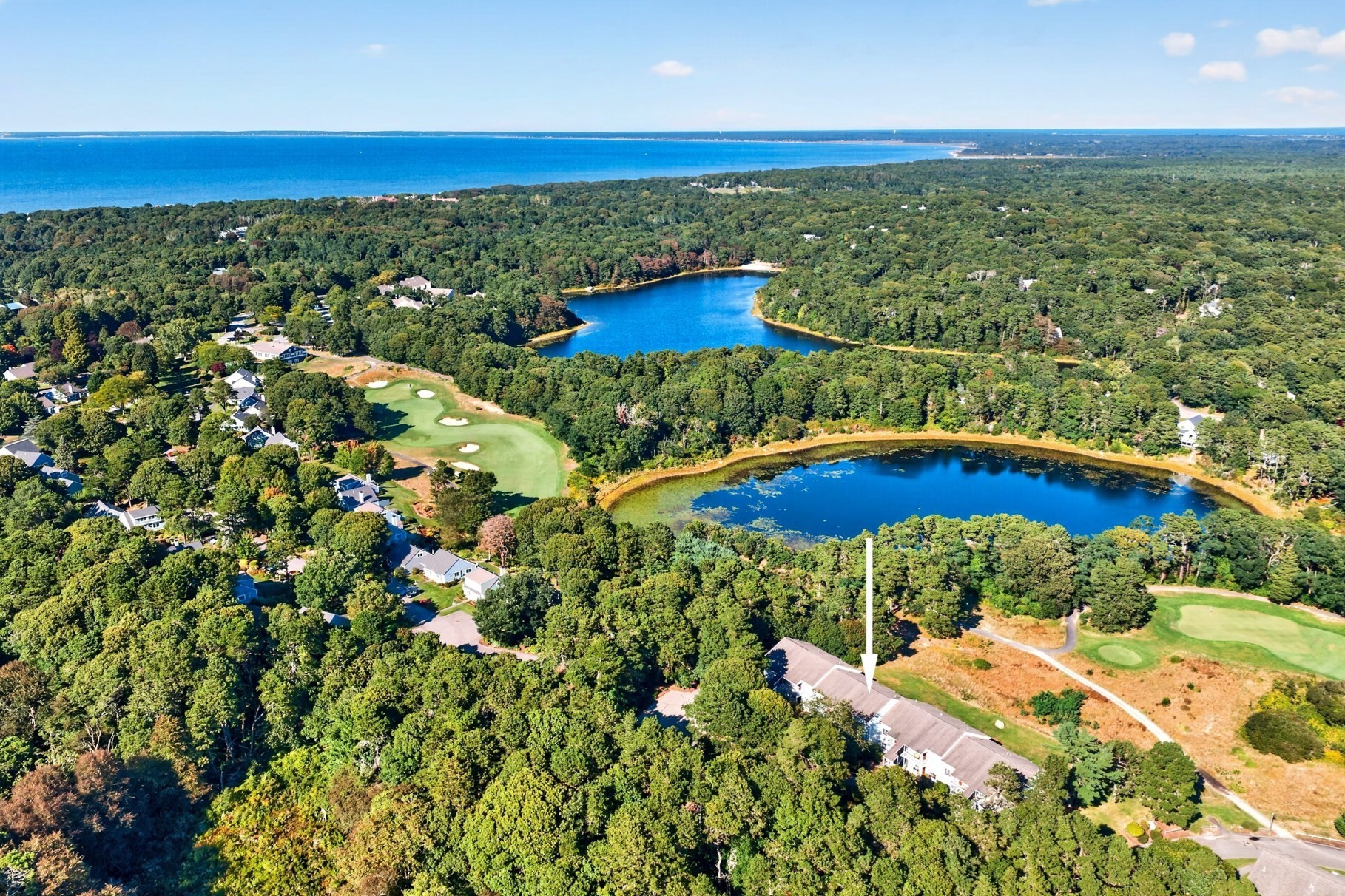 Aerial view of a home marked by an arrow, beside a golf course and wooded ponds.