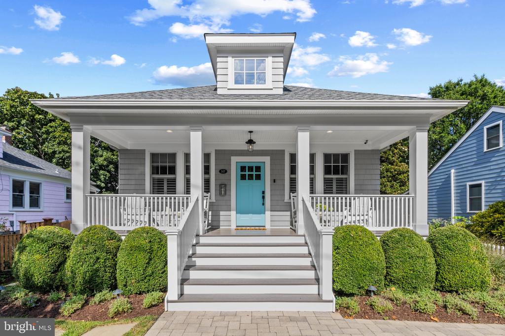 Gray house with a broad white porch, turquoise front door, and clipped shrubs.