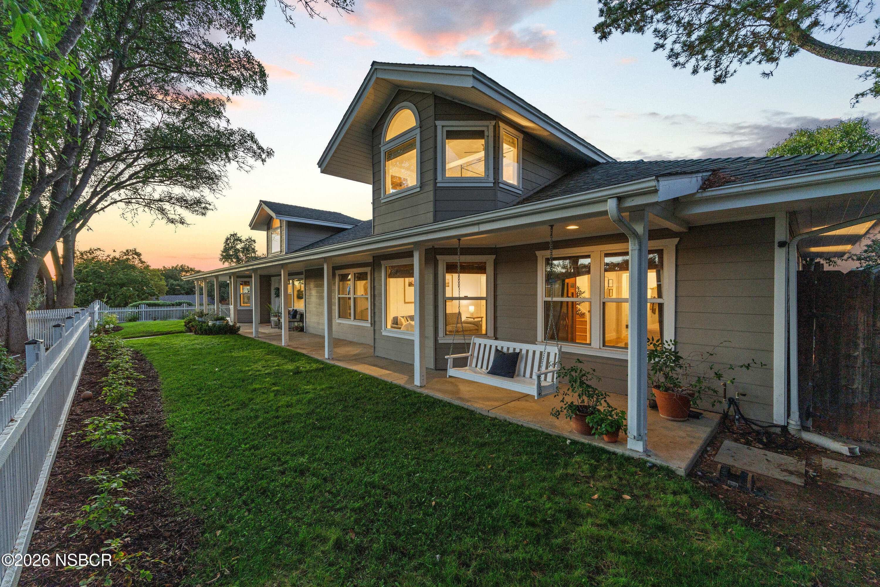Gray two-story home with a covered porch and hanging swing at dusk.