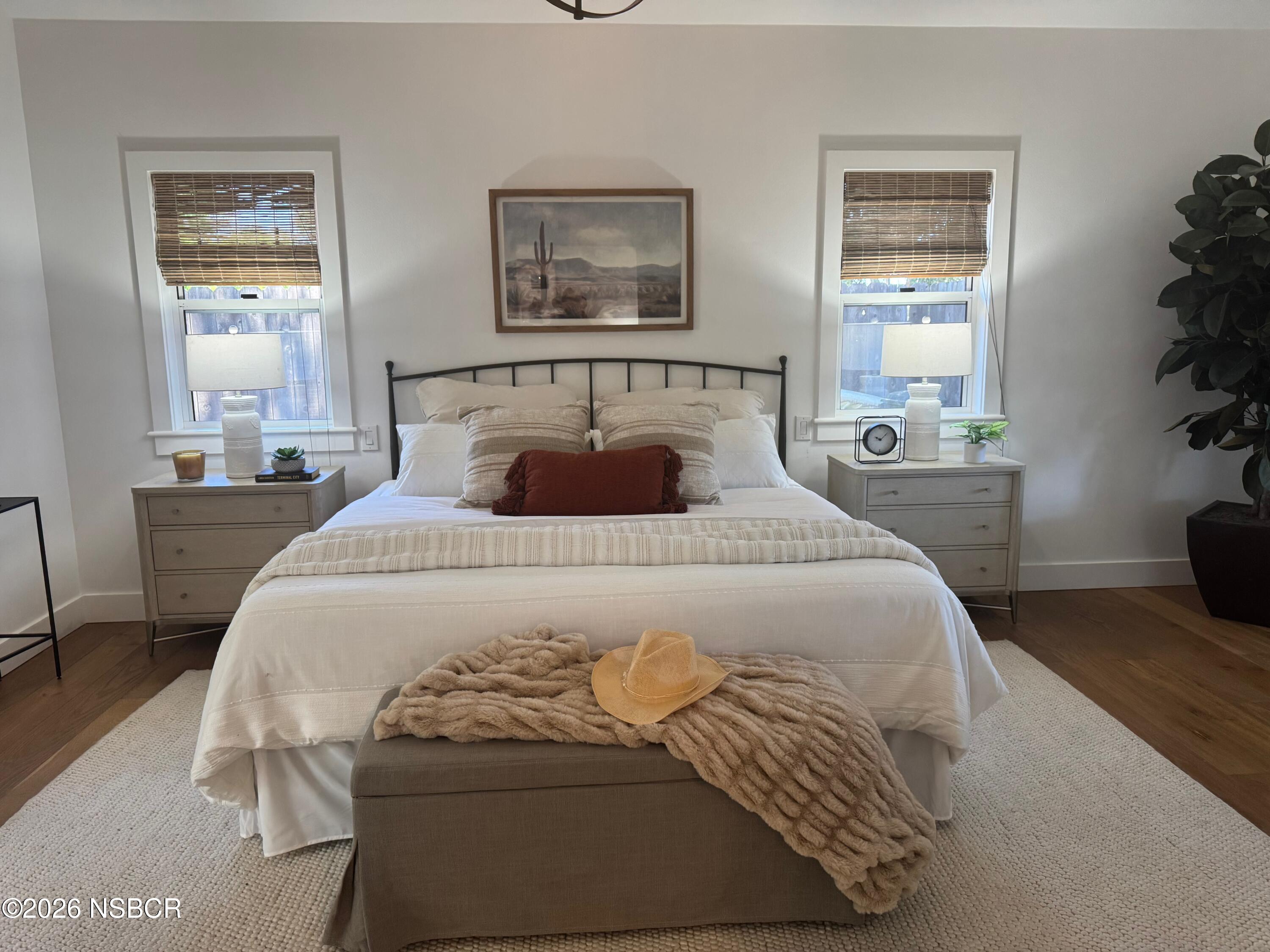 Staged bedroom with a white bed, black metal headboard, matching dressers, and a tan hat on a throw.