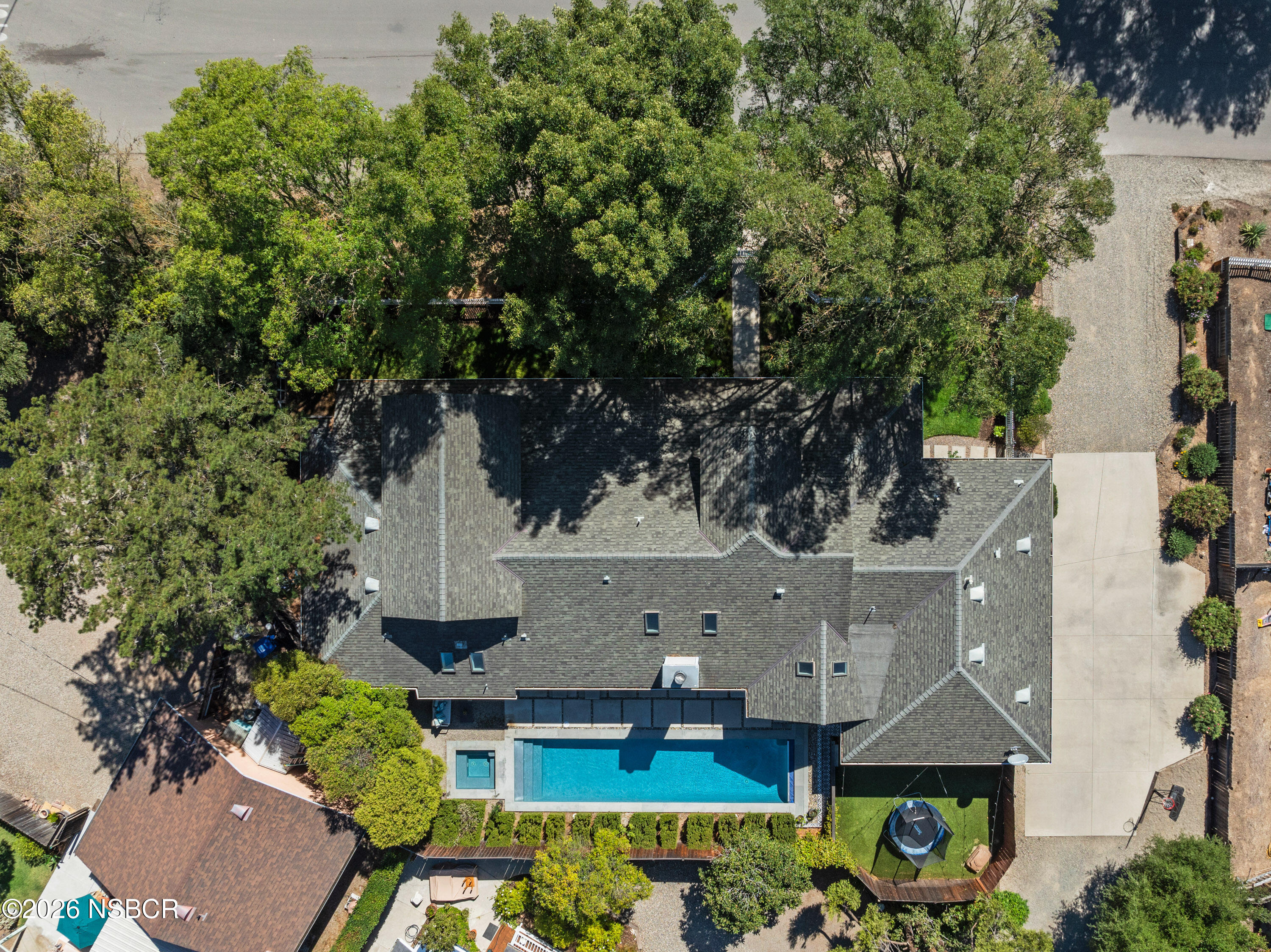 Aerial view of a home with a backyard pool and spa, surrounded by mature trees.