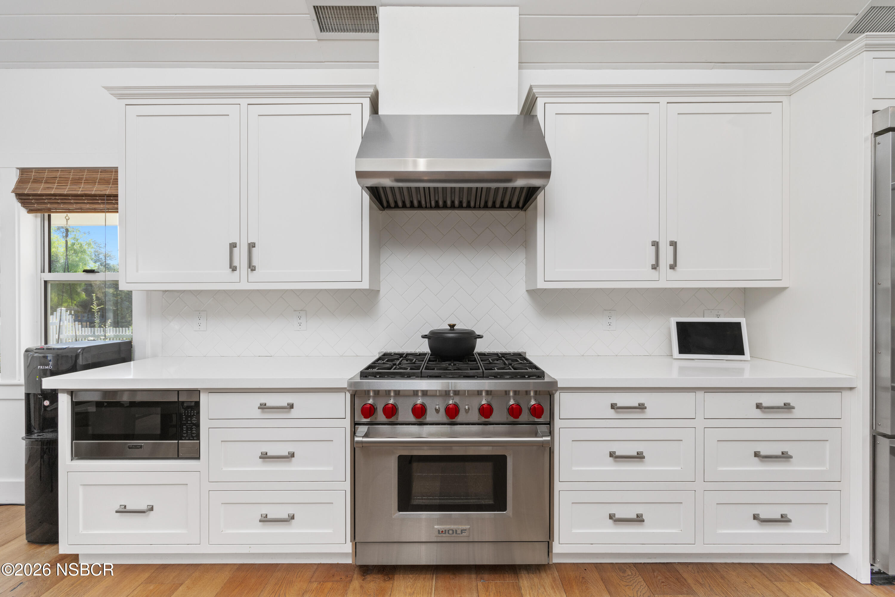 White kitchen with a stainless steel range, red knobs, and a large range hood.