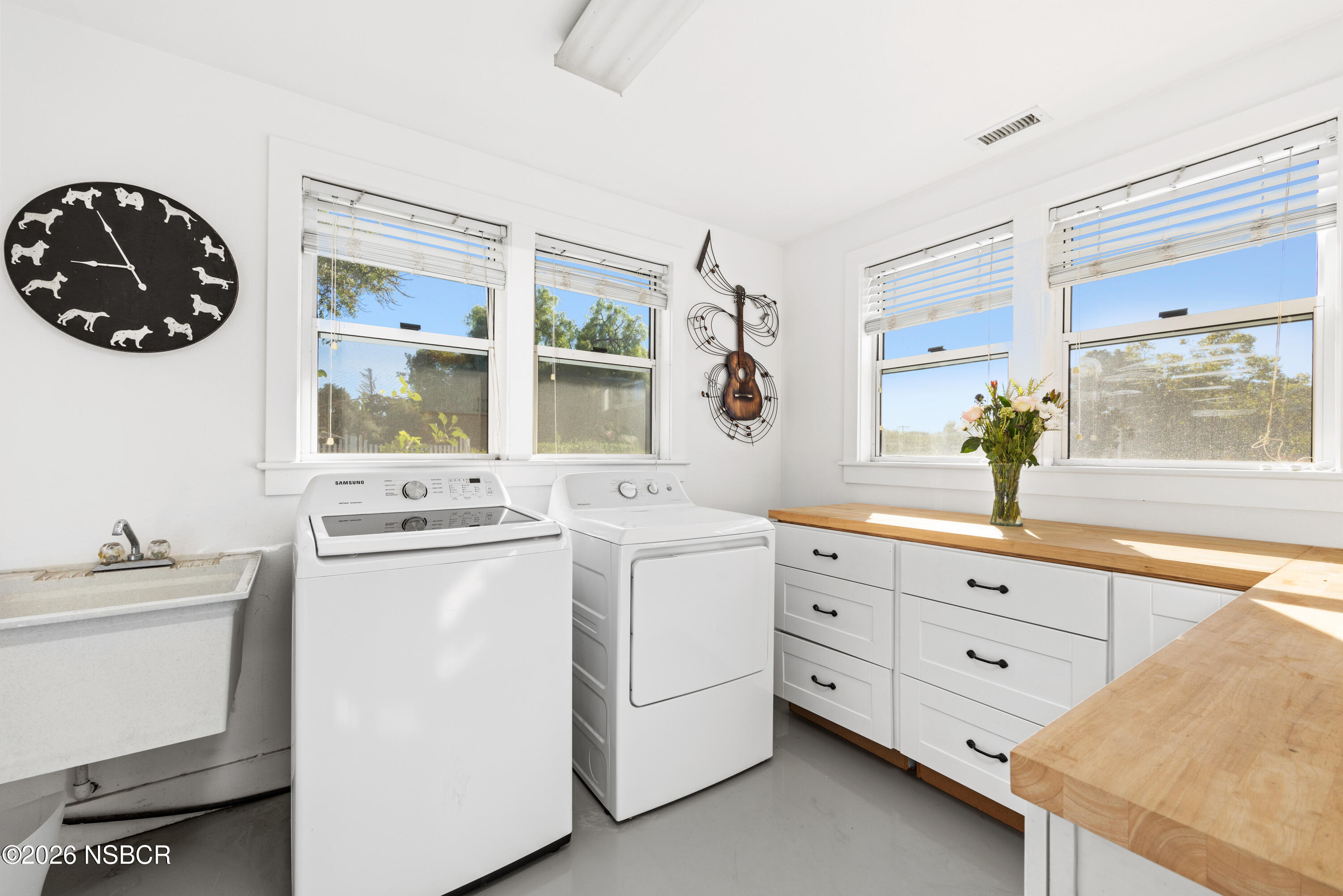 Laundry room with washer and dryer, utility sink, butcher-block counters, and large windows.