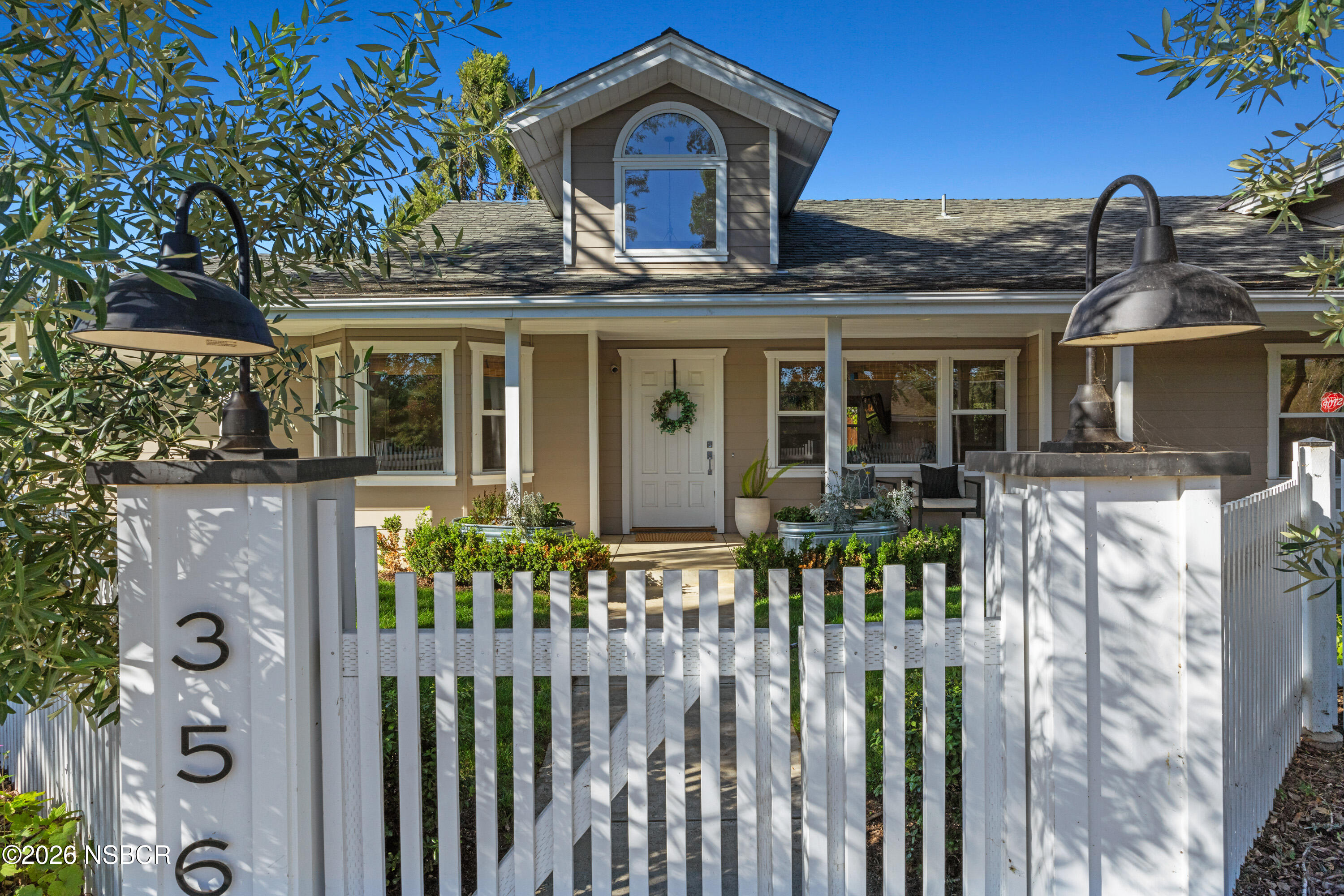 House behind a white picket gate, with oversized black lanterns and an arched dormer window.