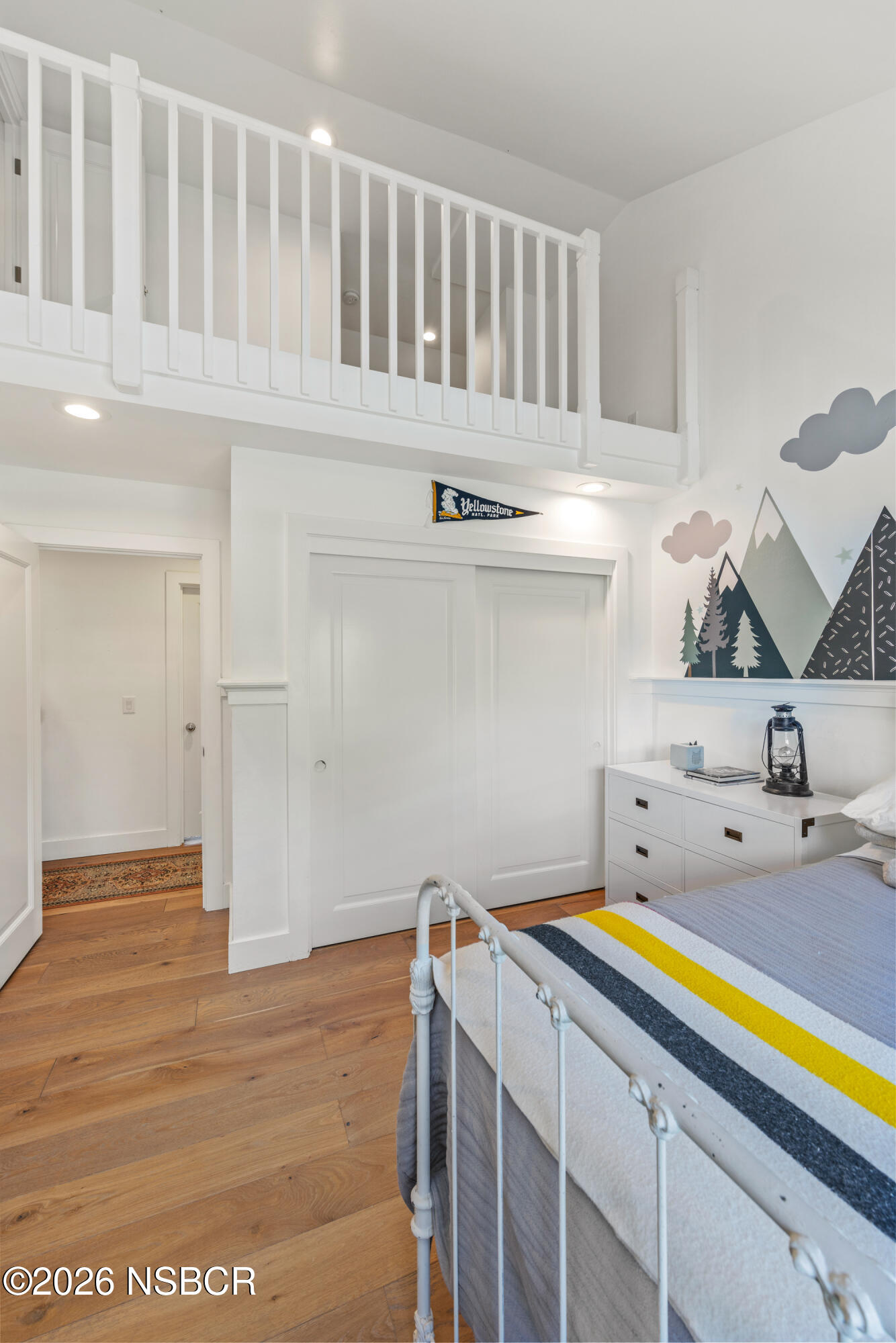 Bedroom with a loft railing, mountain mural, white bed, and warm wood flooring.