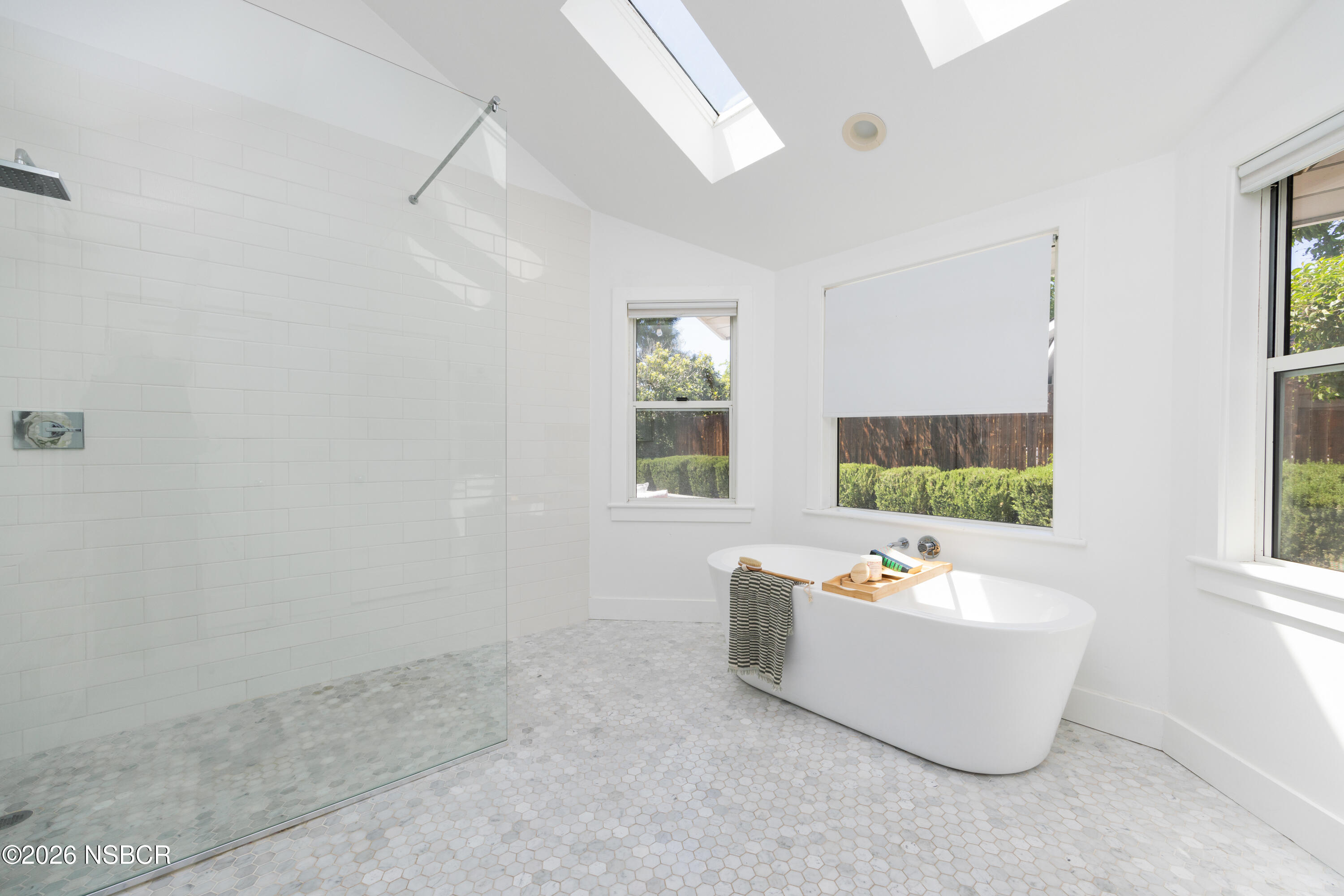 Bright bathroom with a freestanding soaking tub beside a glass shower and large windows.