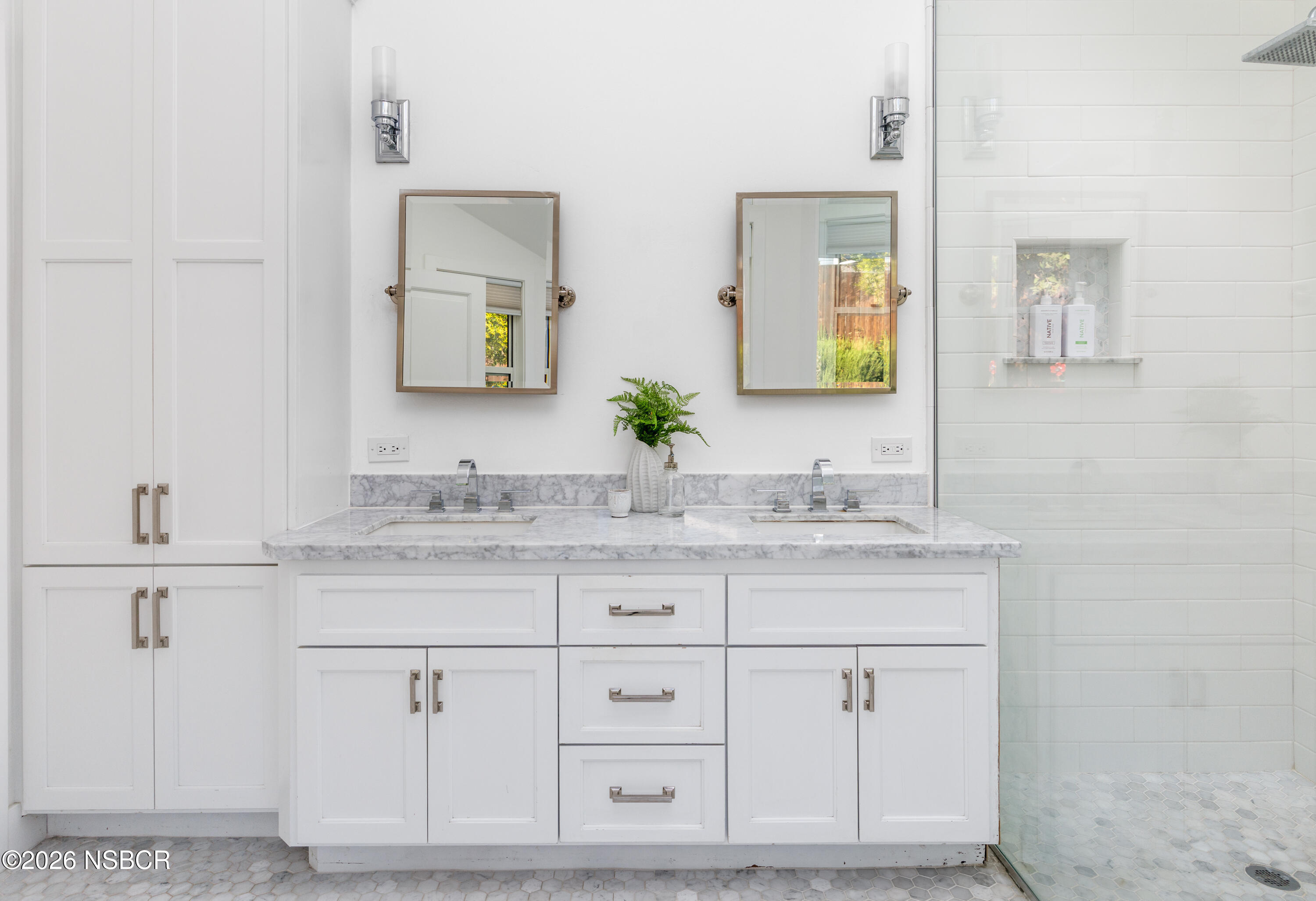 Bathroom with a white double vanity, marble counter, paired mirrors, and a tiled walk-in shower.