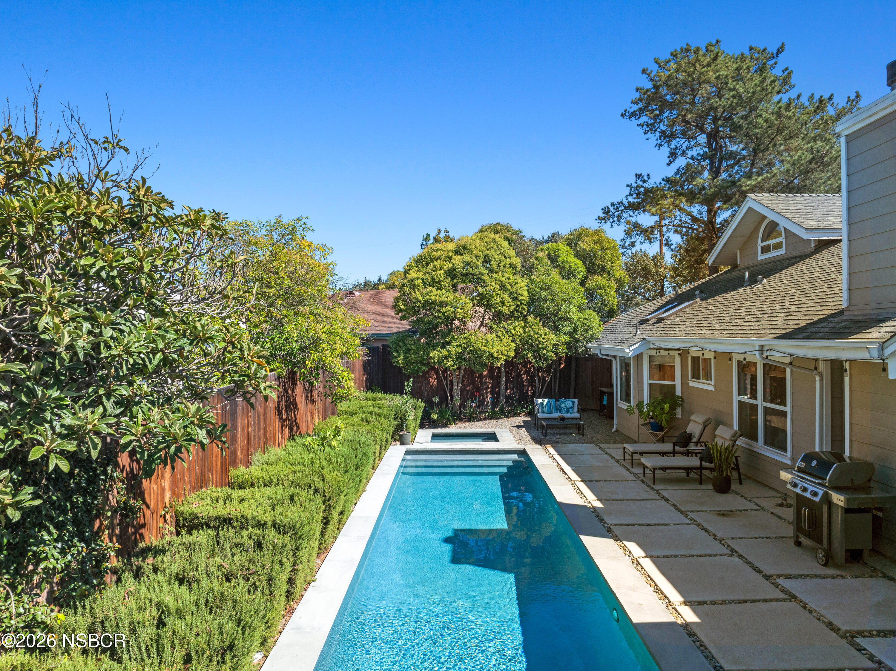 Backyard pool and spa beside a paved patio with lounge chairs and a grill.
