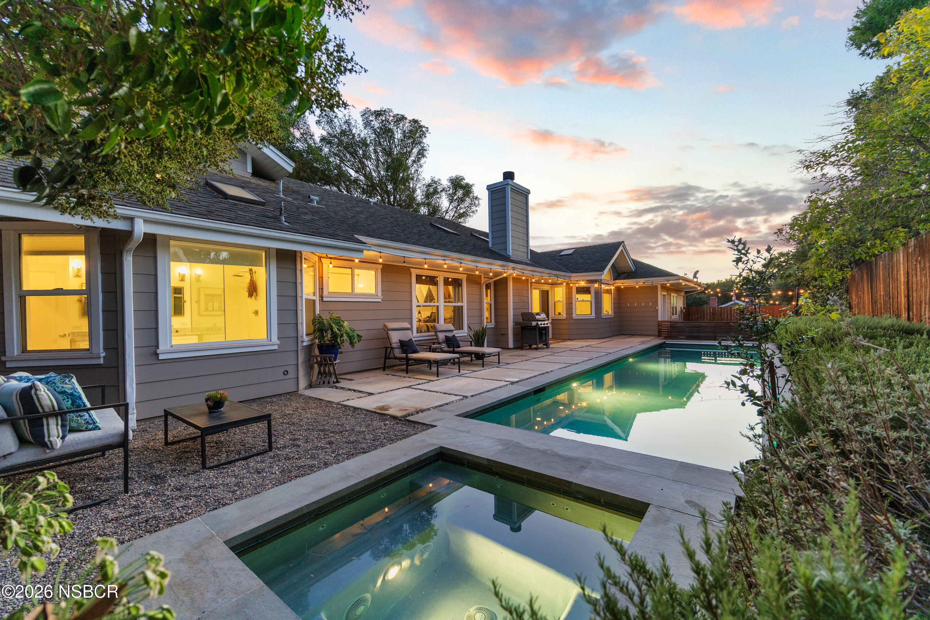 Home’s rear patio and swimming pool at dusk, with string lights and a small spa.