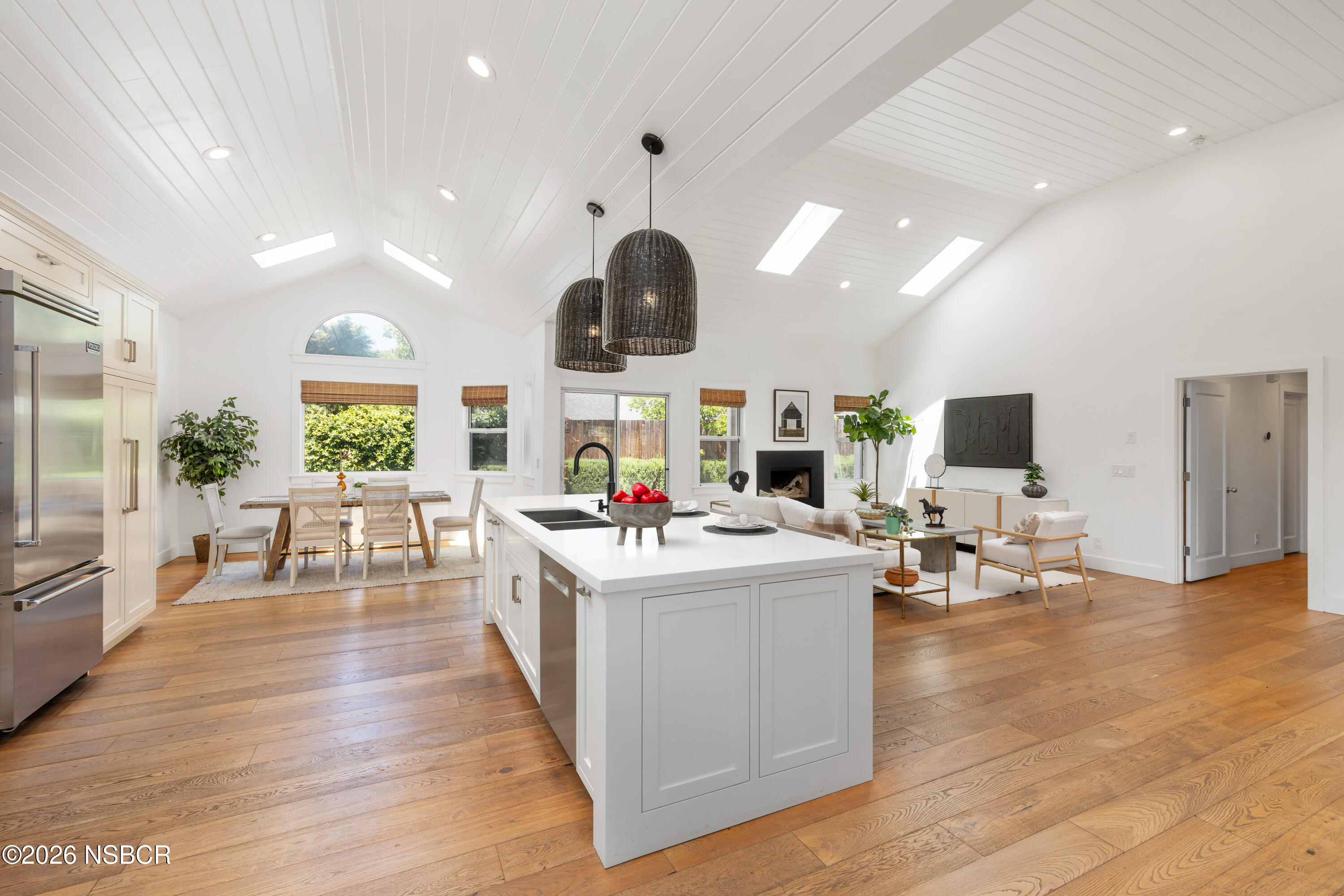 Open-plan kitchen with a large white island, wood floors, vaulted ceiling, and adjoining living area.