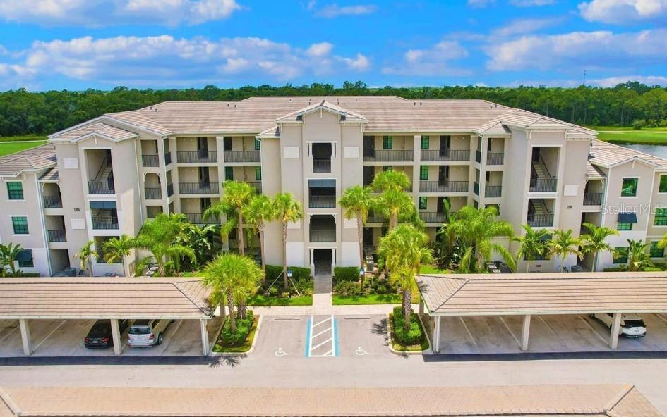 Aerial view of a condominium building with palm trees, balconies, and covered parking.