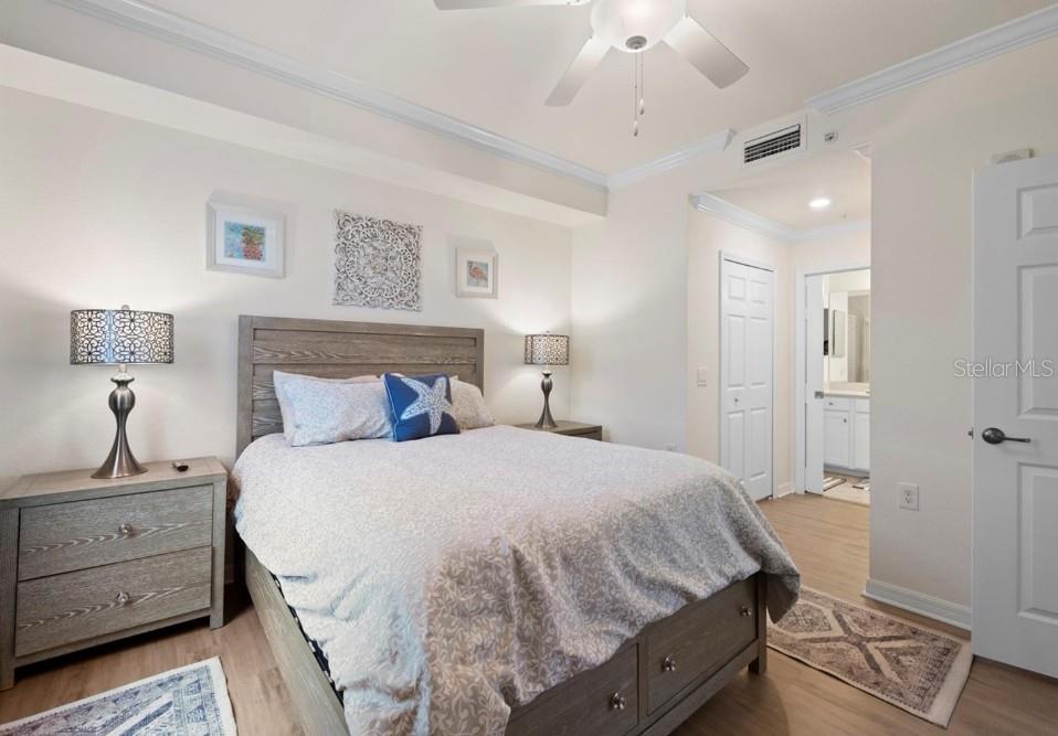 Furnished bedroom with a gray wood bed, blue accent pillows, and an adjoining bathroom doorway.