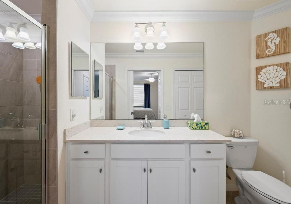 Bathroom with white vanity, wide mirror, glass-enclosed tiled shower, and toilet.