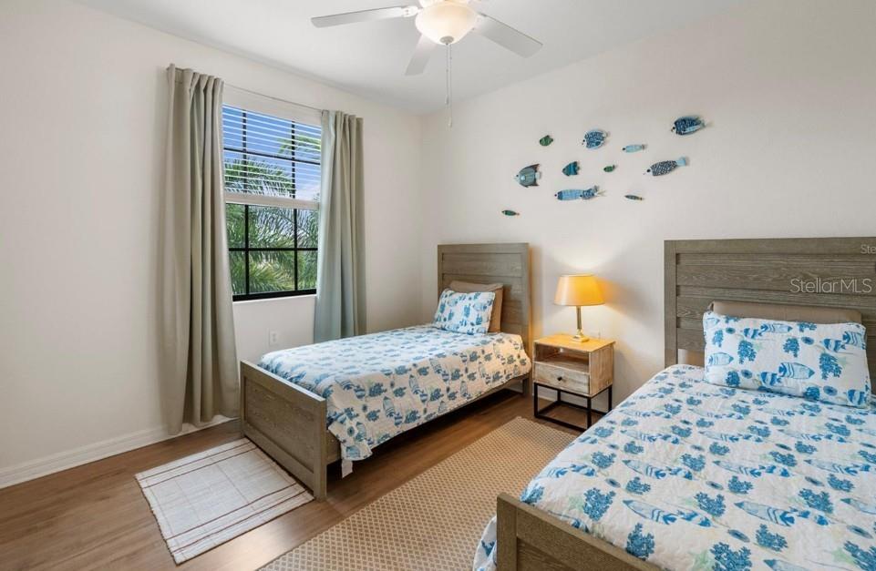 Bedroom with twin beds, blue patterned bedding, fish wall decorations, and a window overlooking palm foliage.