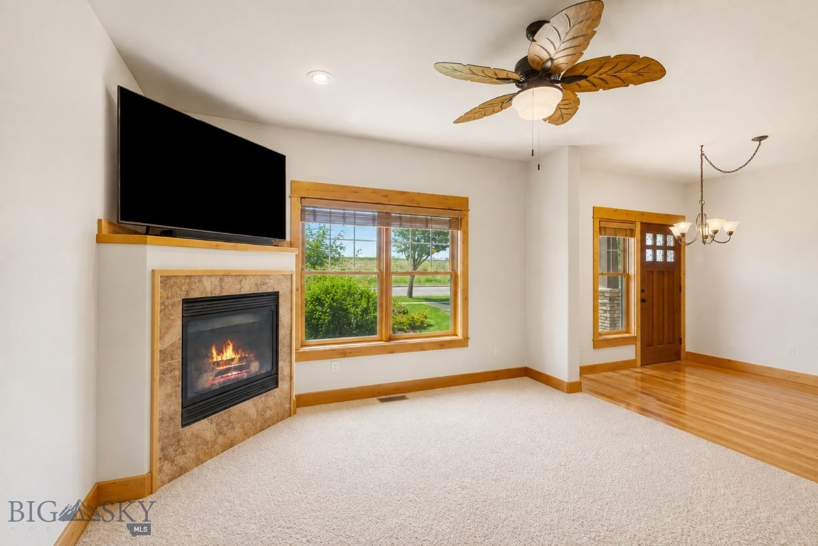 Living room with a stone fireplace, mounted television, large windows, and leaf-shaped ceiling fan.
