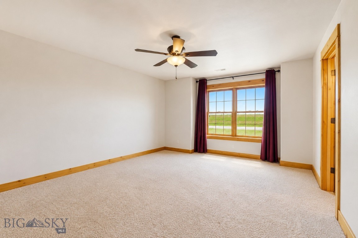Empty carpeted bedroom with a ceiling fan and a large window overlooking a green field.