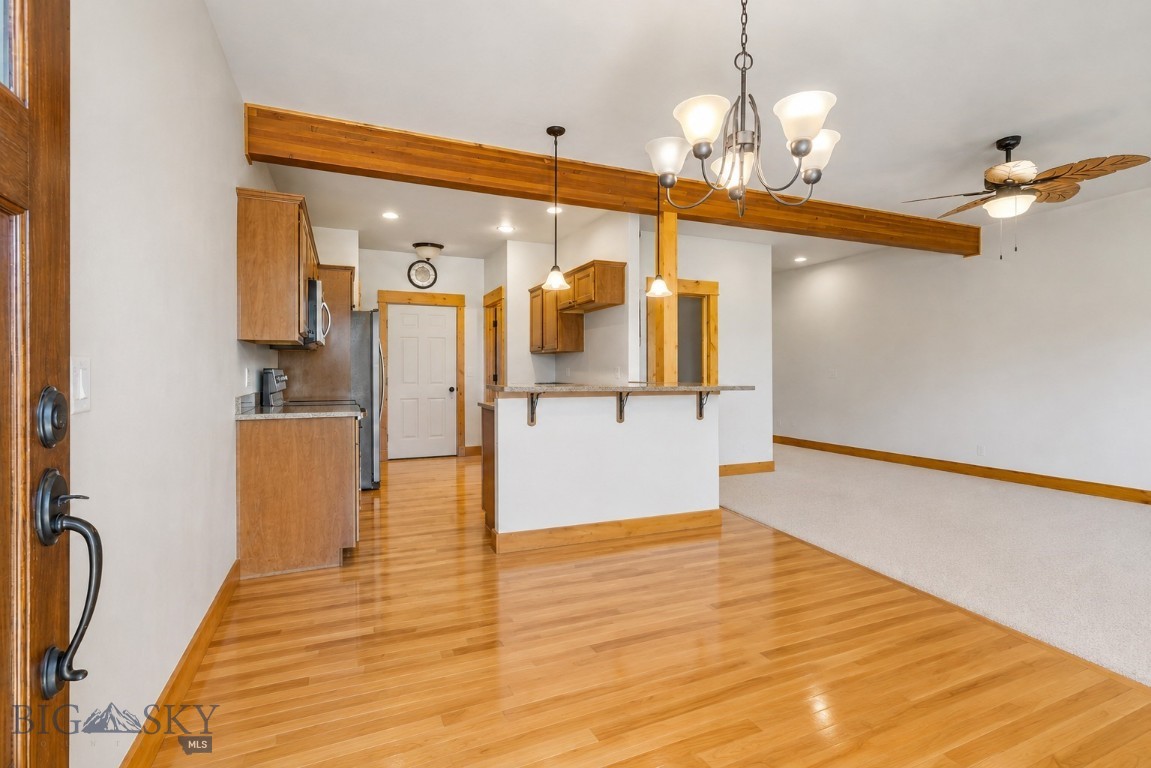 Open kitchen and dining area with wood cabinetry, hardwood floors, breakfast bar, and exposed beam.