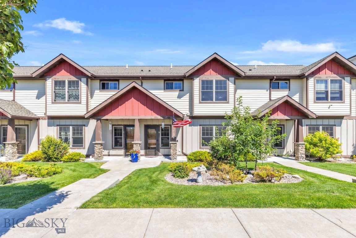 Attached townhouse with red gables, stone porch columns, landscaped lawn, and a U.S. flag.