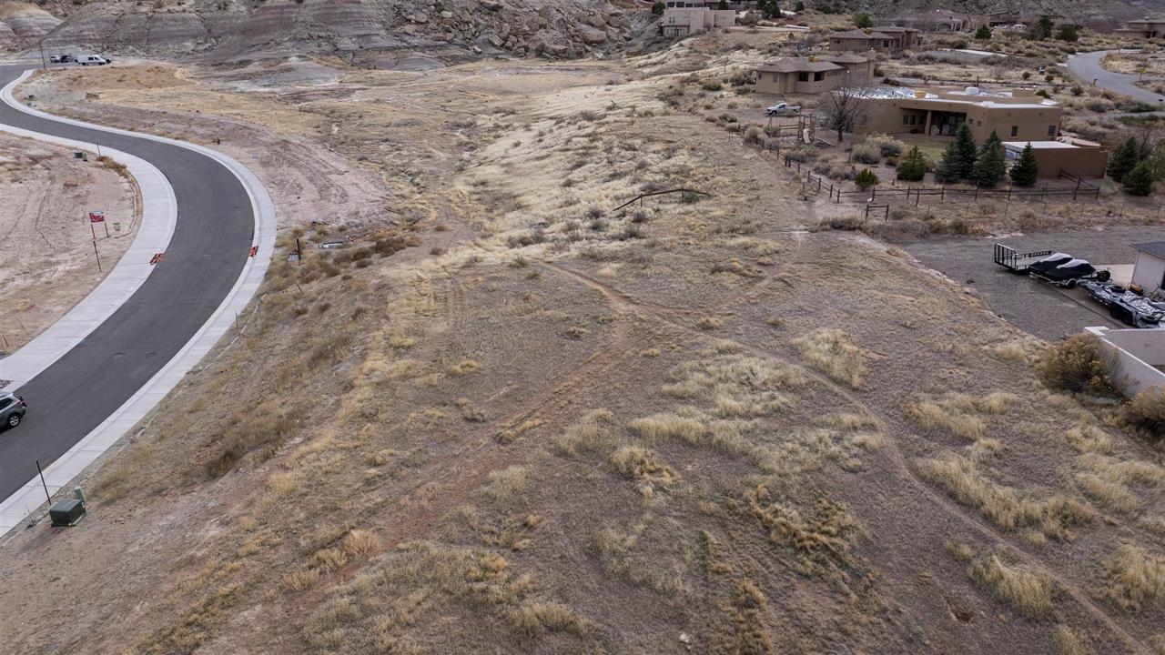 Aerial view of a vacant desert lot beside a curving paved road and nearby homes.