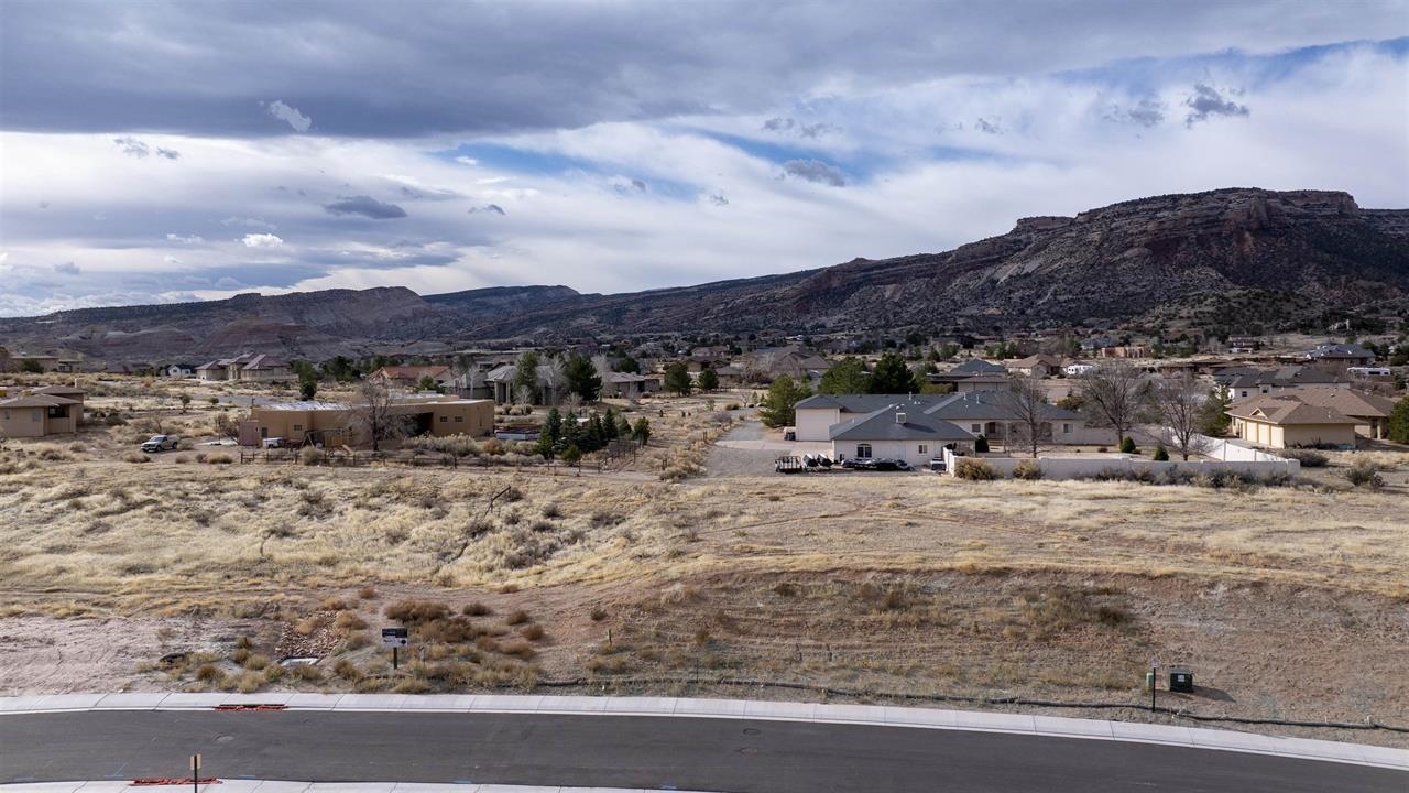 Vacant residential lot with dry scrub, neighboring homes, and rugged mesas beyond.