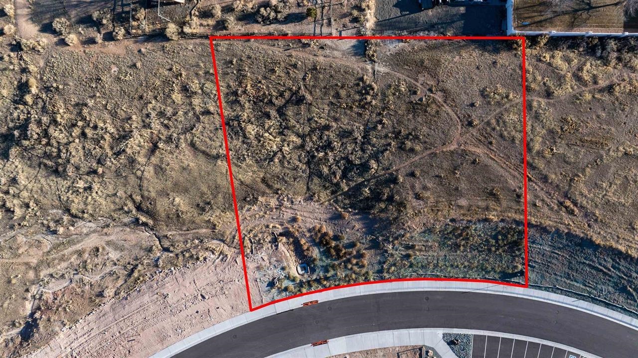 Aerial view of a vacant lot outlined in red beside a curved paved road.