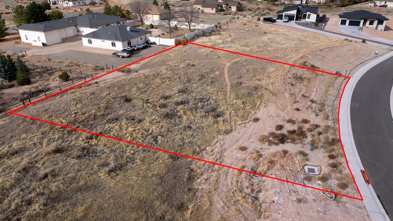 Aerial view of a vacant lot outlined in red beside a curved residential street.