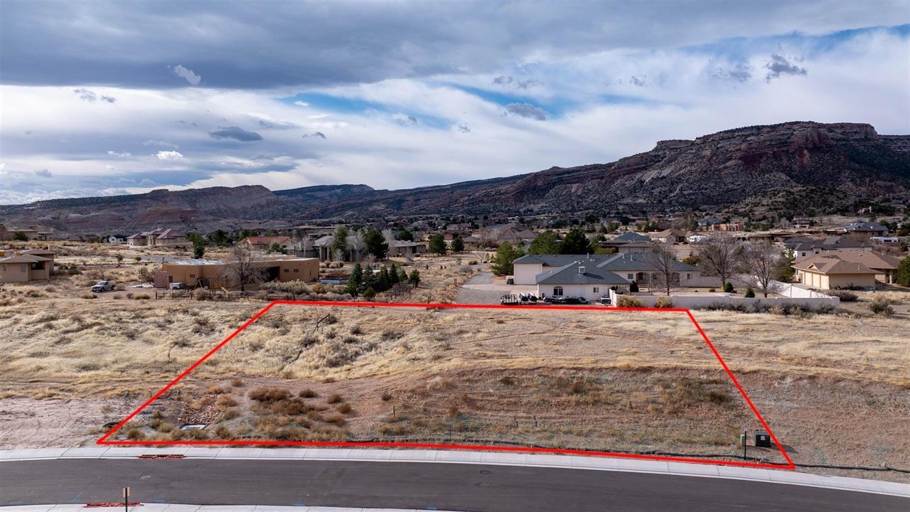 Vacant lot outlined in red, with neighborhood homes and rocky mesas behind it.