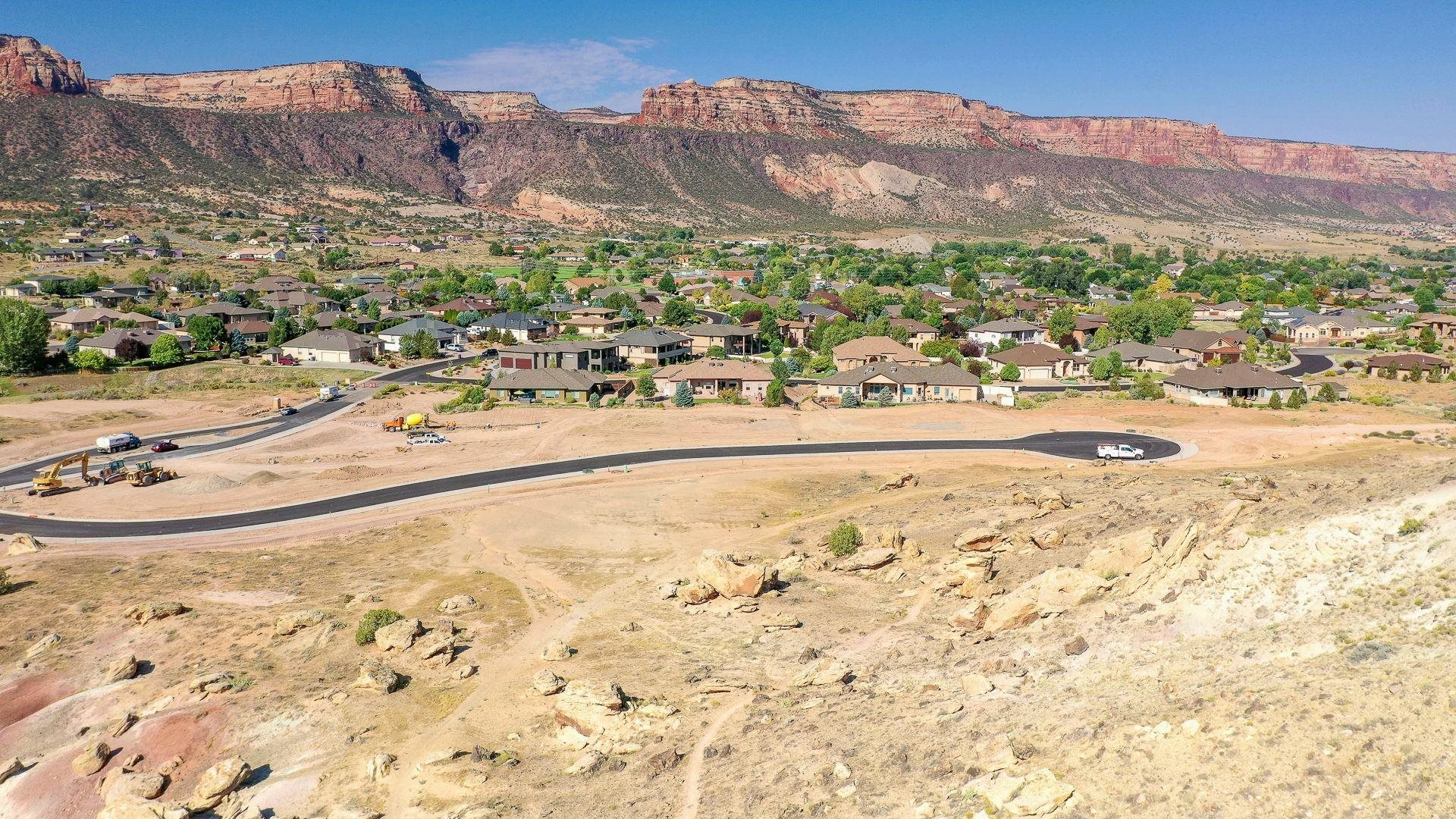 Aerial view of a neighborhood beside red rock cliffs, with new road construction in the foreground.
