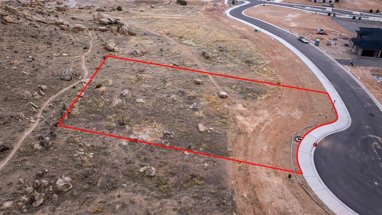 Vacant rocky lot outlined in red beside a curving paved street.
