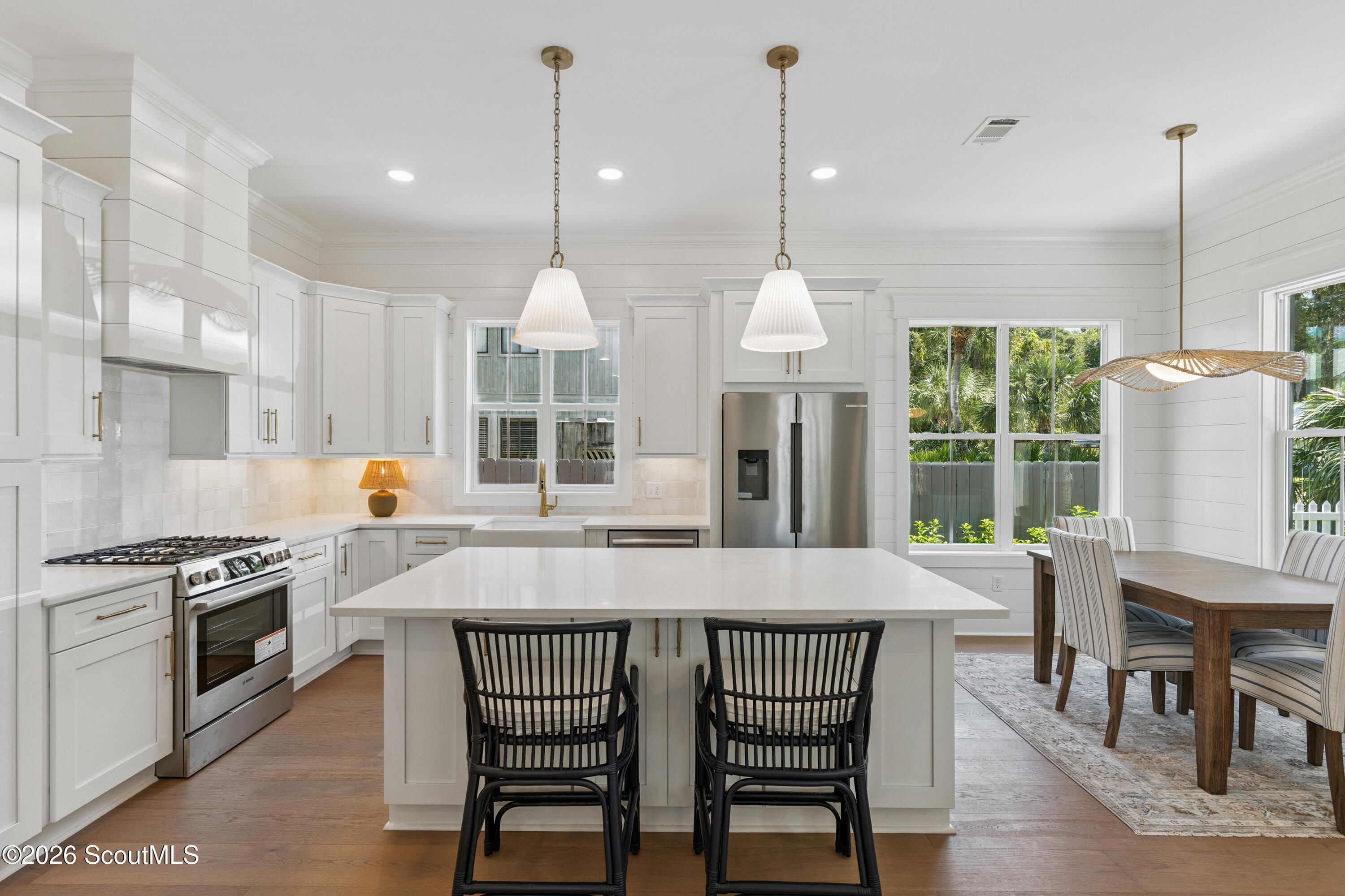 Bright white kitchen with a large island, stainless steel appliances, and an adjoining dining area.