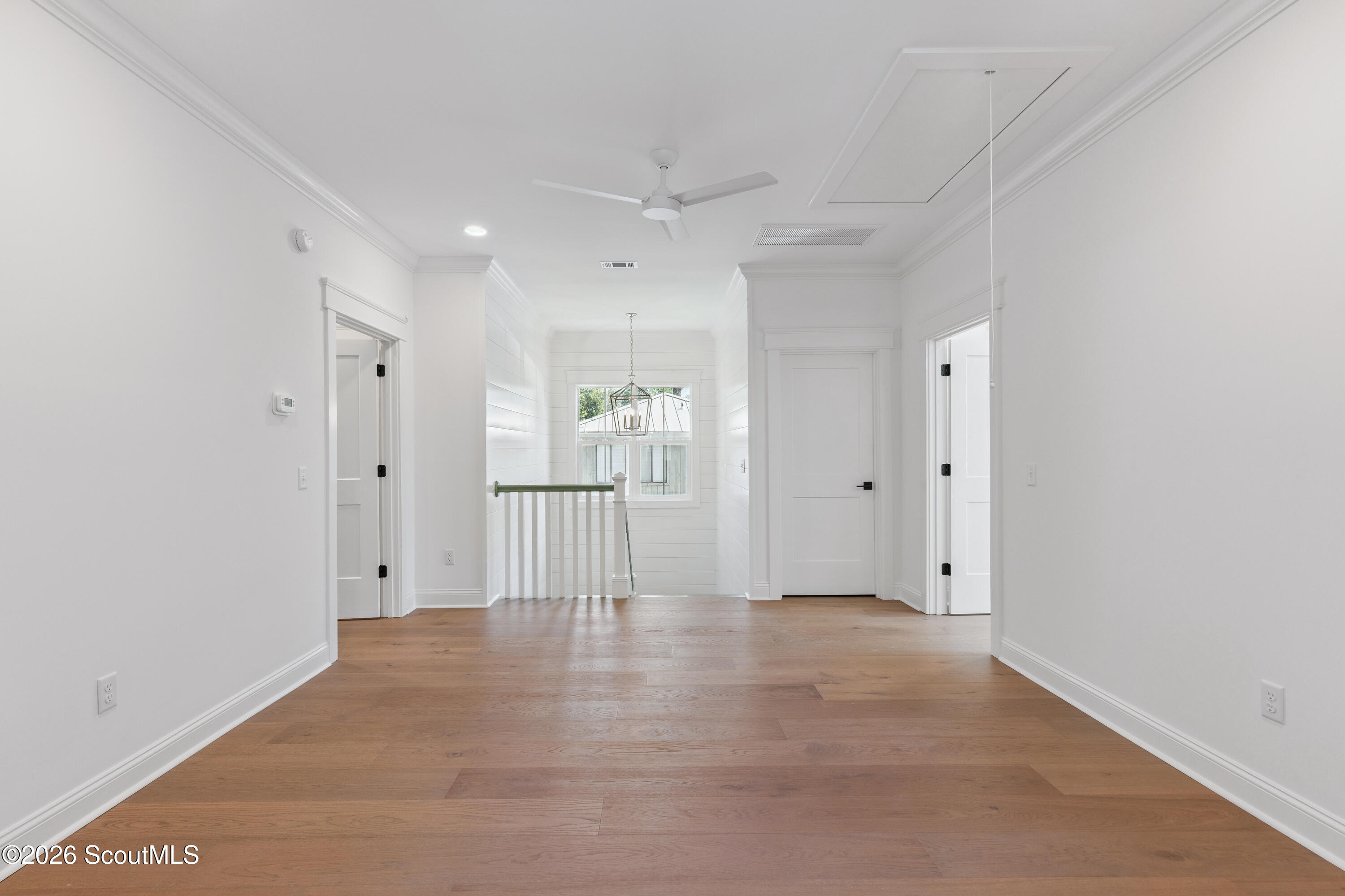Bright, empty hallway with warm hardwood floors, white paneled walls, and a railing beside the stair opening.