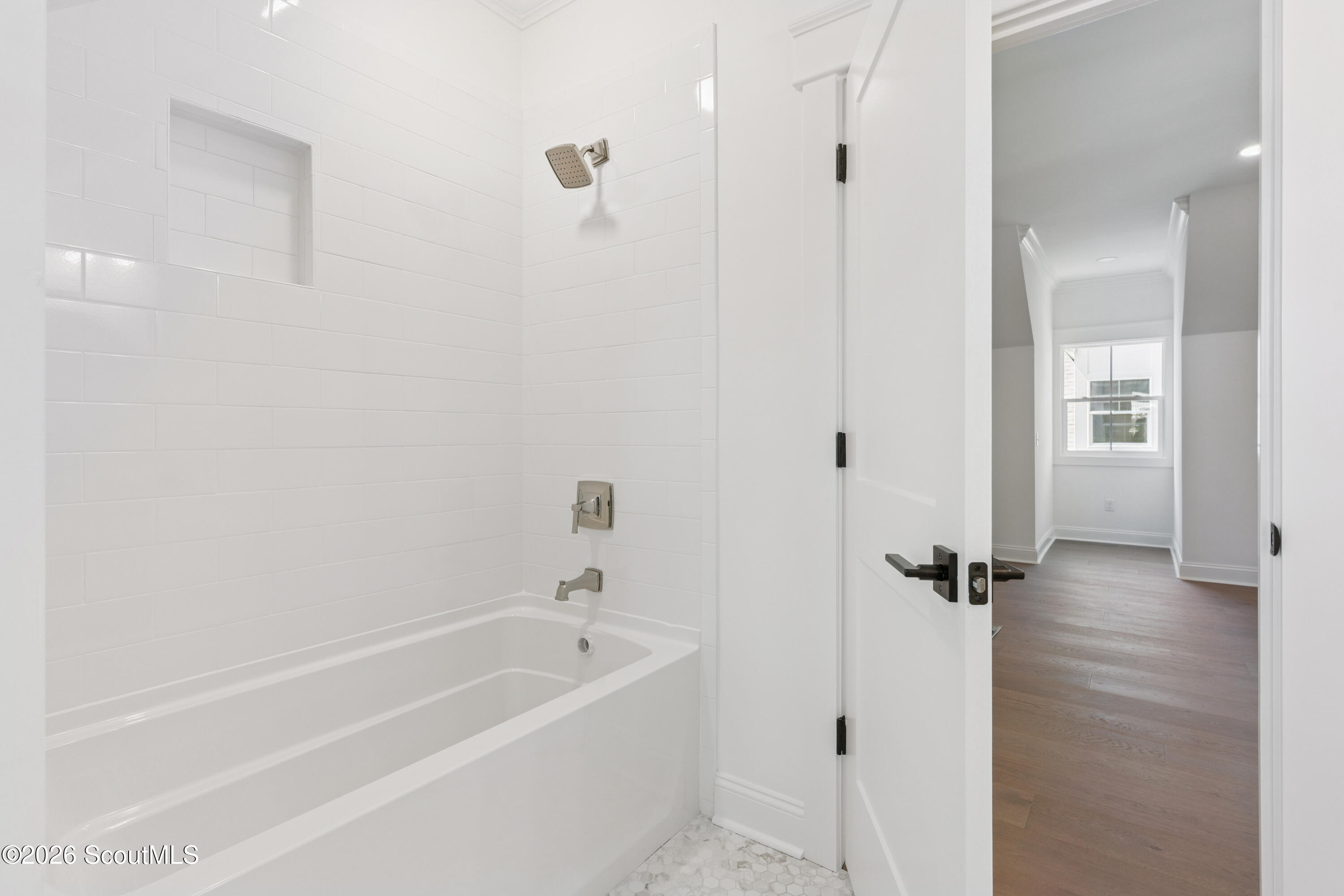 Bathroom with white subway tile around a bathtub and an open door to a wood-floored hallway.
