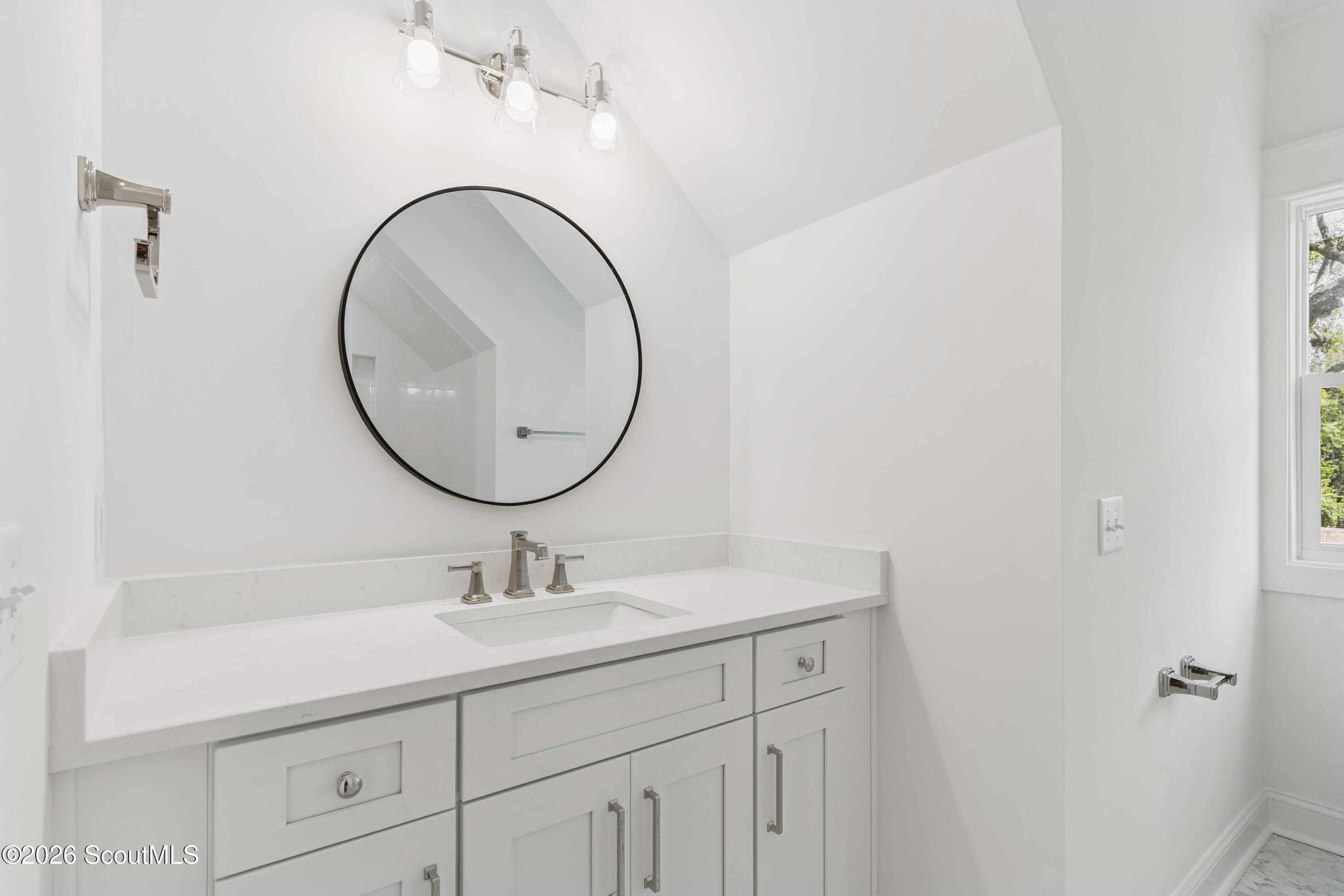 Bathroom vanity with a quartz countertop, round black-framed mirror, and white paneled cabinets.