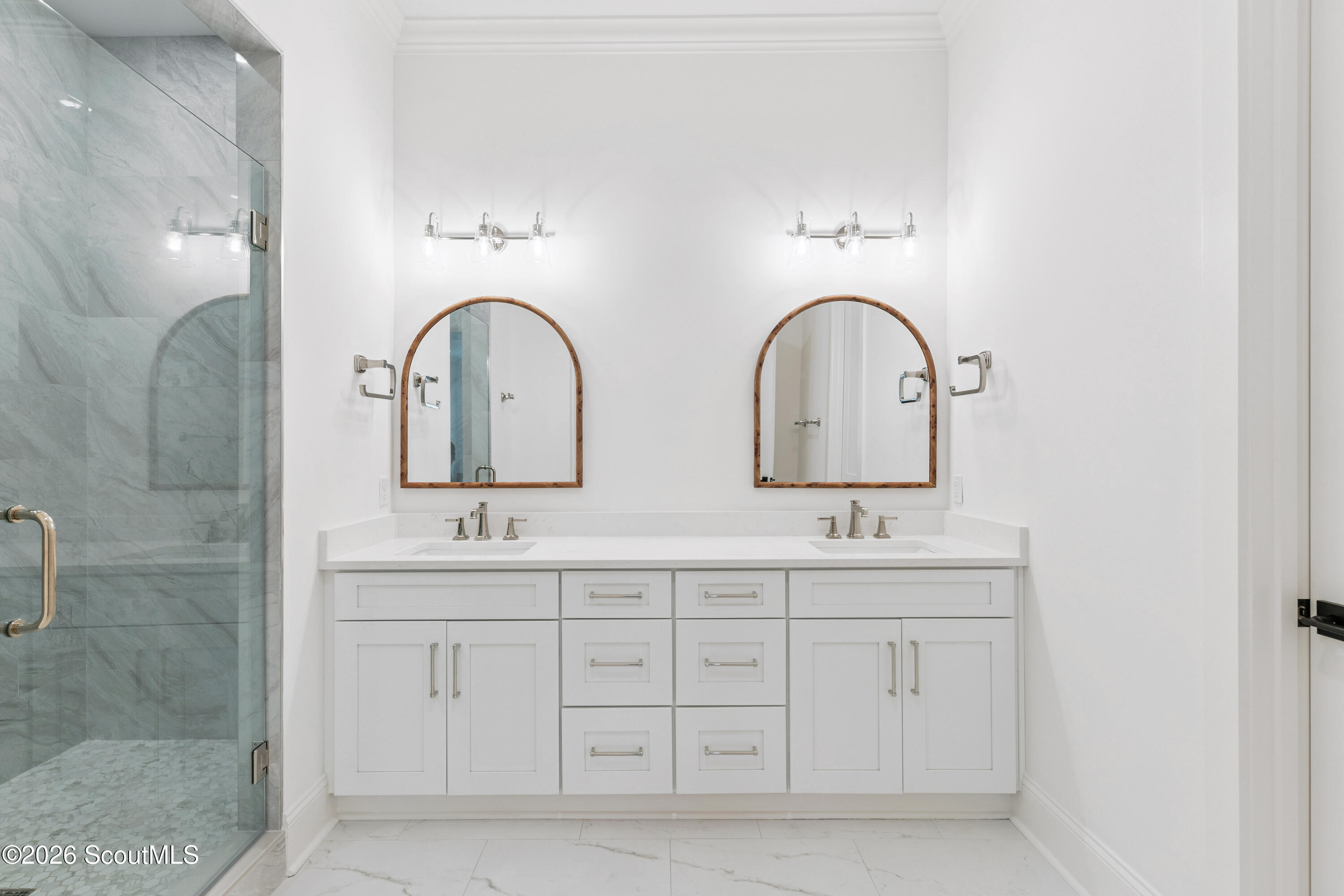 Bathroom with a white double vanity, arched wood-framed mirrors, and a marble-look glass shower.