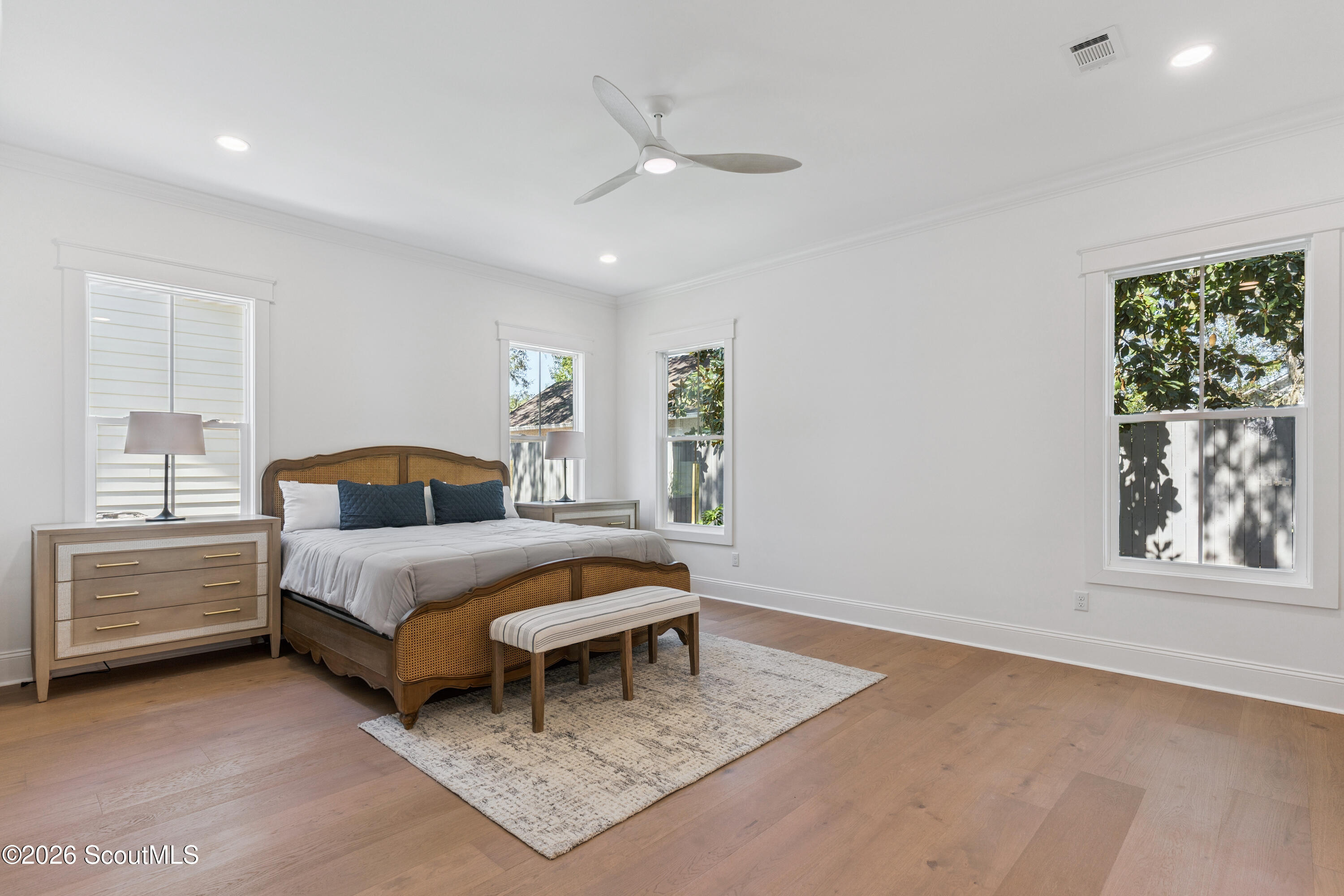 Bedroom with a cane-panel bed, navy pillows, a striped bench, and light wood floors.