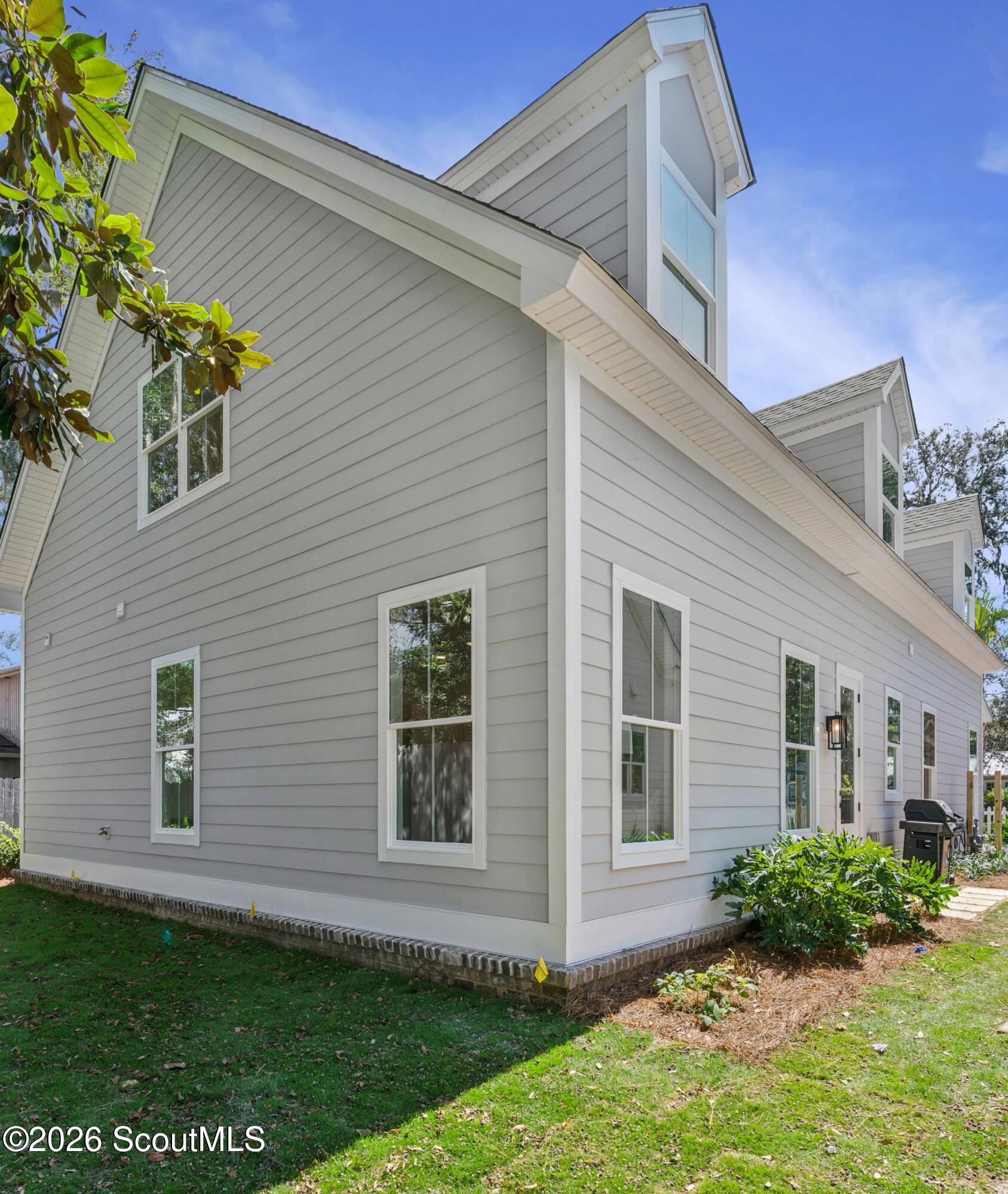Light gray multi-gabled house with white trim, viewed from the side across a green lawn.