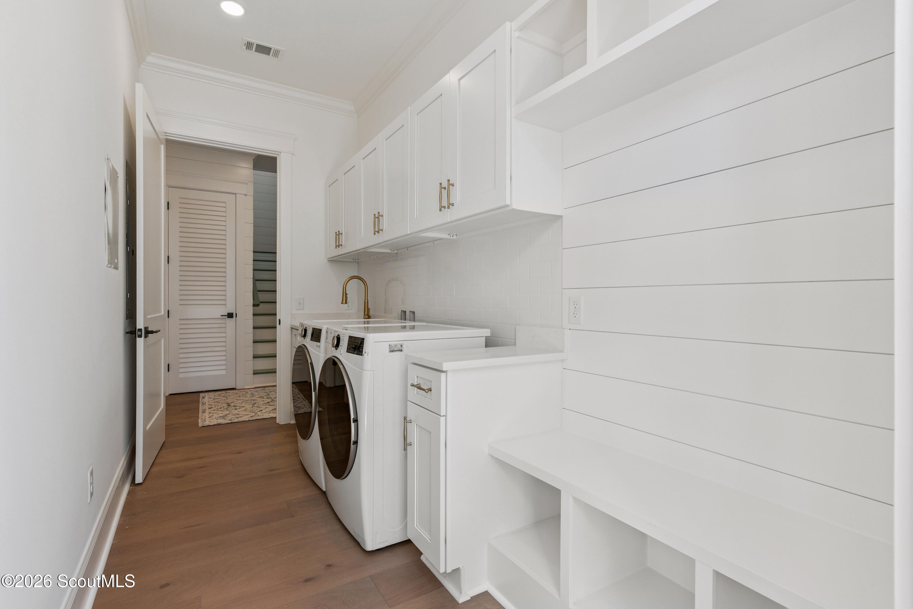 Laundry room with front-loading washer and dryer, white built-ins, and a shiplap wall.