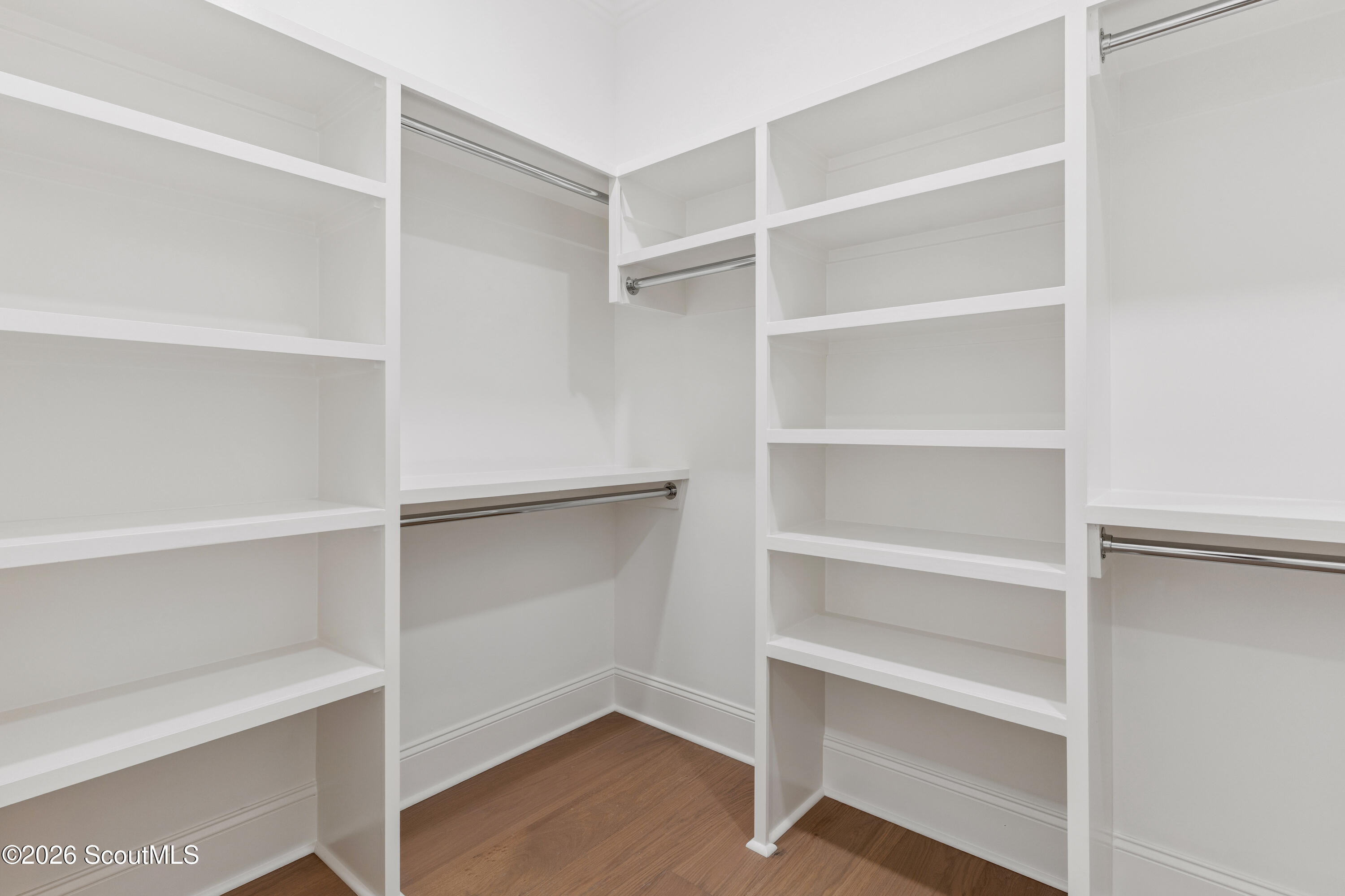 Walk-in closet with white built-in shelves, metal hanging rods, and wood flooring.
