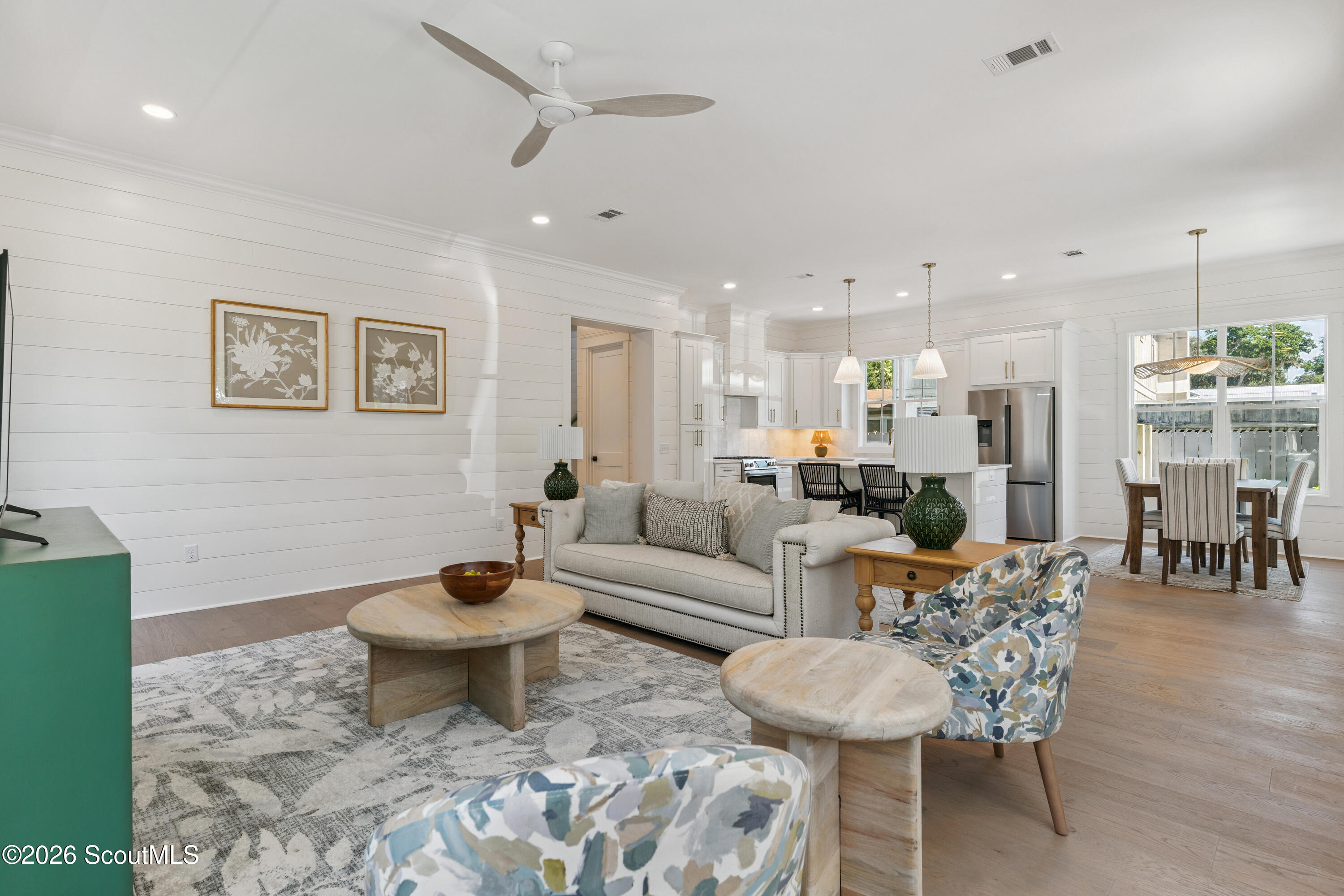 Open-plan living room with neutral seating, white shiplap walls, and the kitchen and dining area beyond.