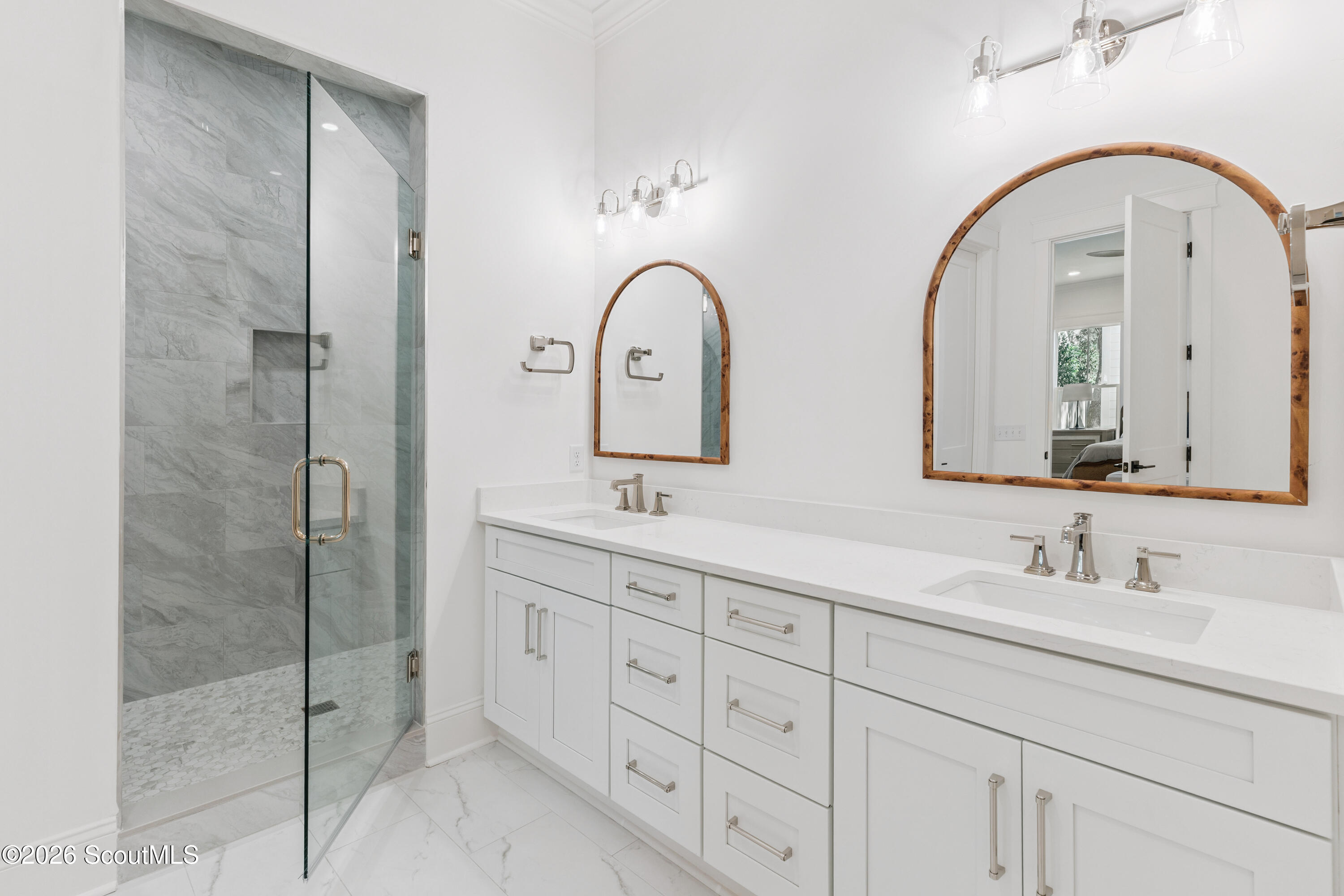 Bathroom with double vanity, arched wood-framed mirrors, and glass-enclosed marble shower.