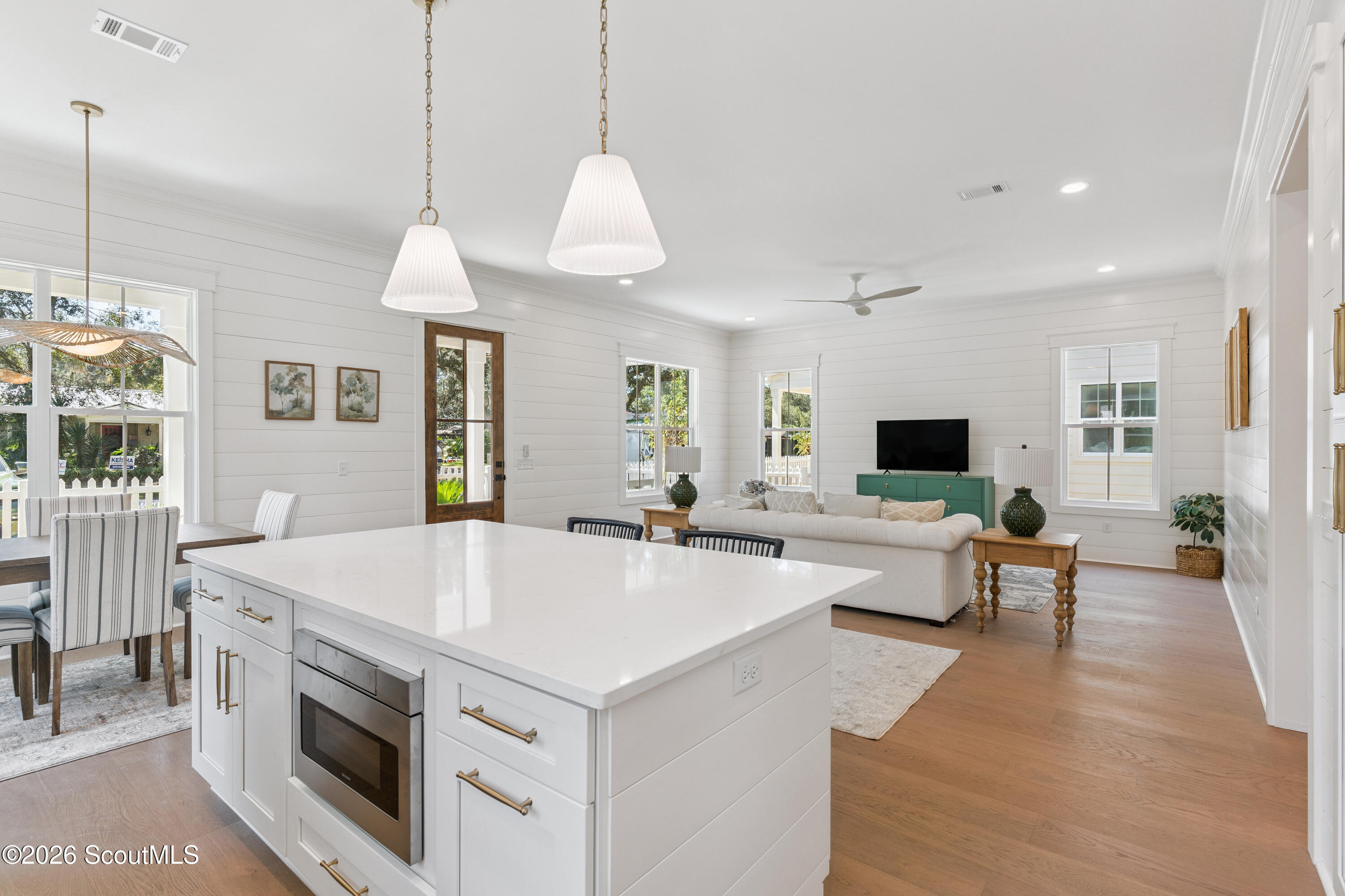 Open-plan kitchen and living room with a large white island, wood floors, and bright windows.