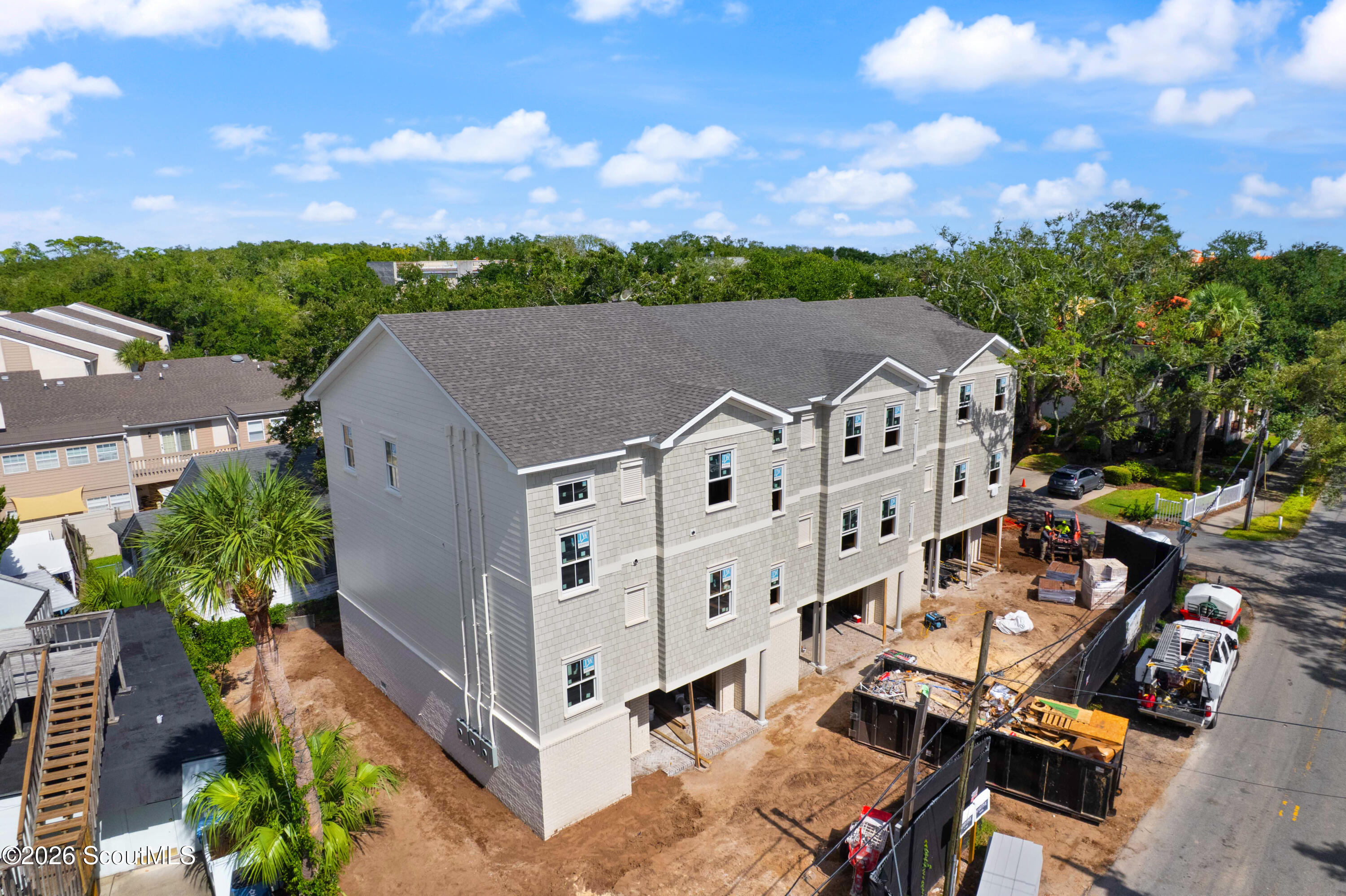 Aerial view of a gray multi-story building under construction, with equipment and neighboring homes.