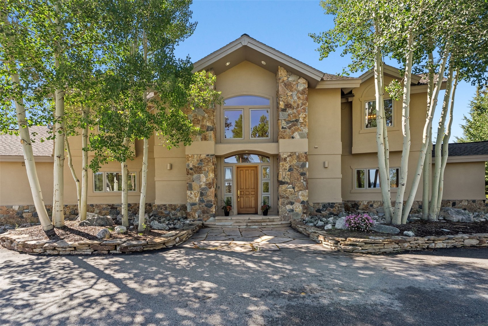 Two-story tan home with a stone-accented entry, aspen trees, and a flagstone walkway.