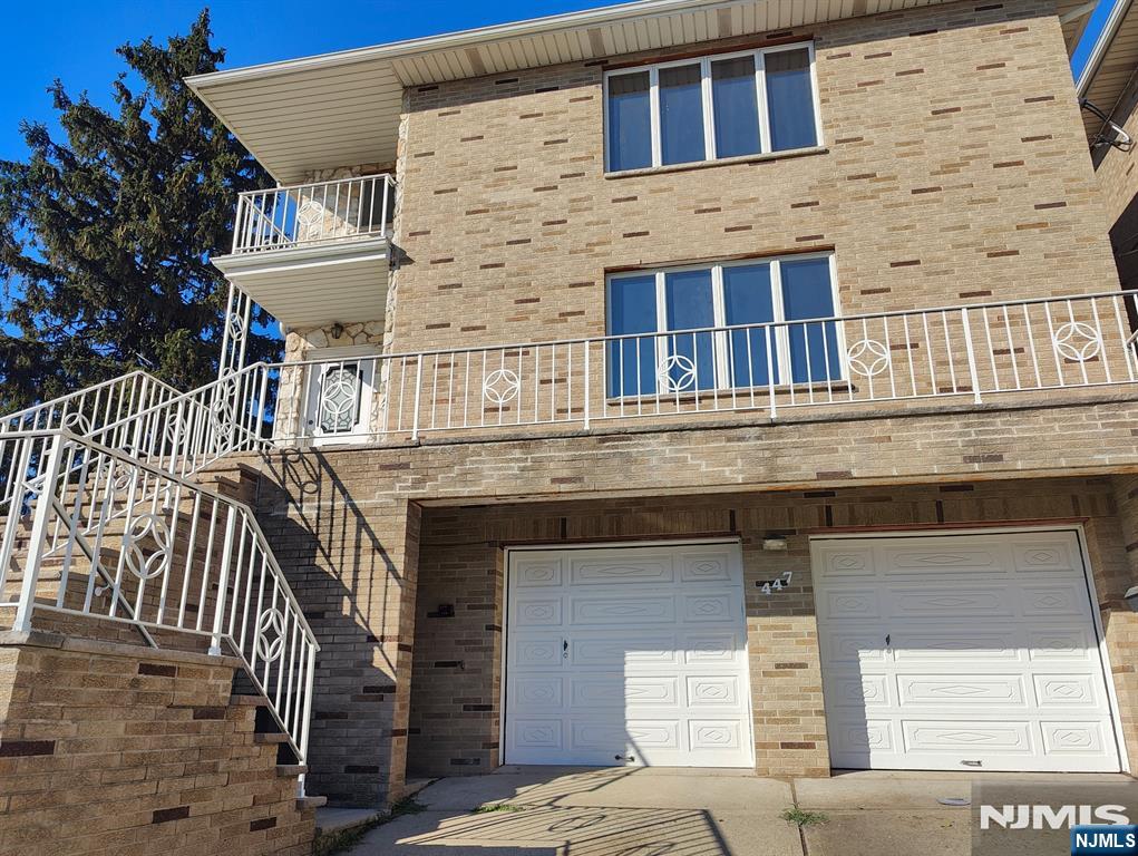 Tan brick home with white balconies, an exterior staircase, and two garage doors.
