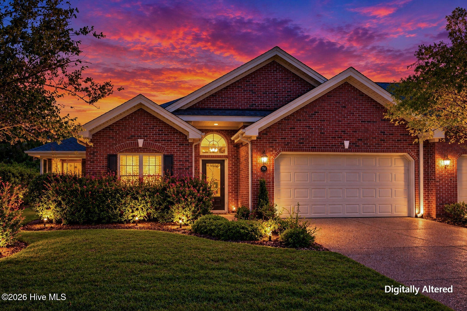 Red brick home with a two-car garage and landscaped yard glowing beneath a colorful sunset.